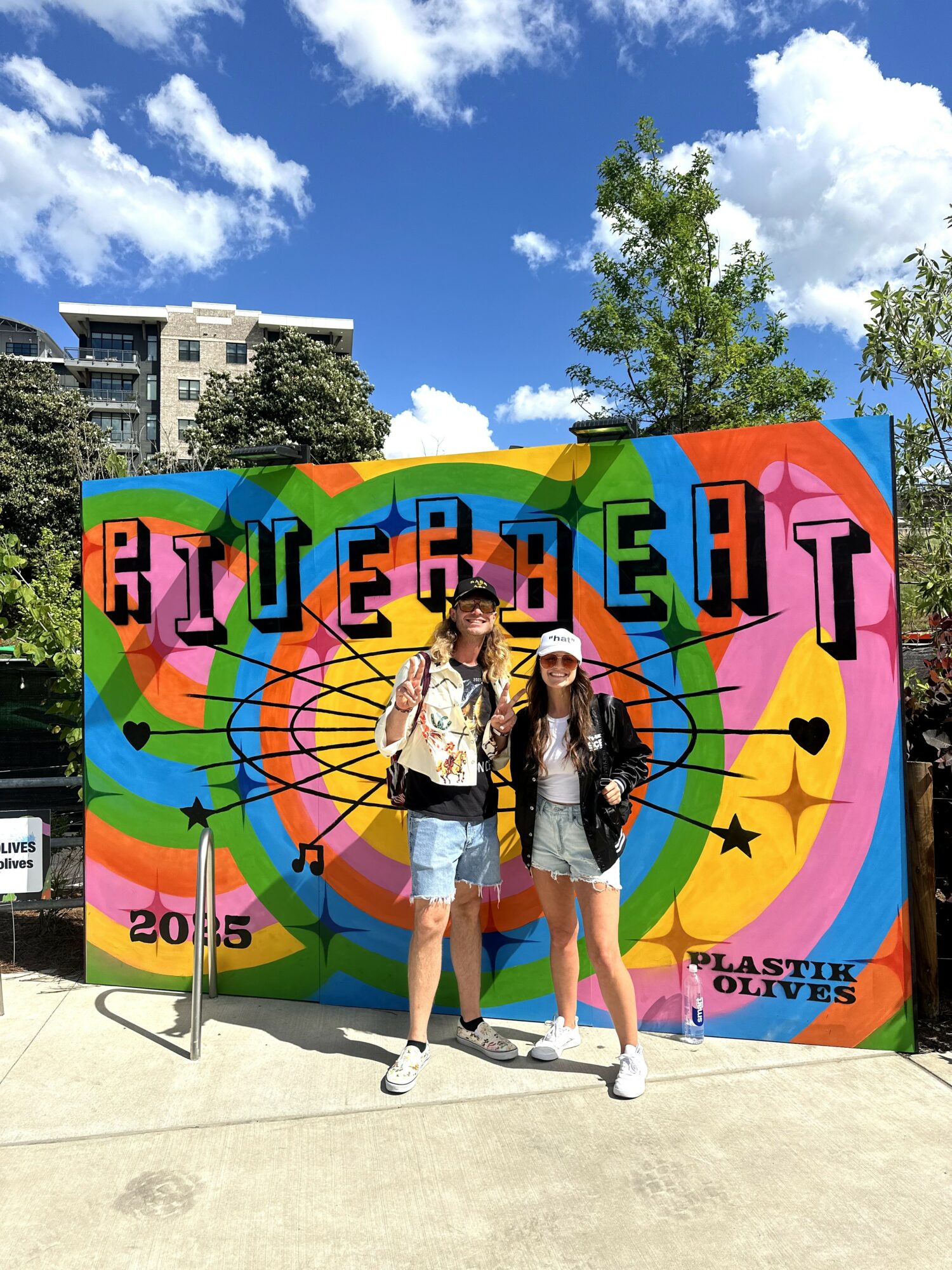 Two people stand in front of a colorful mural with abstract shapes and the word 'BLUE' visible.