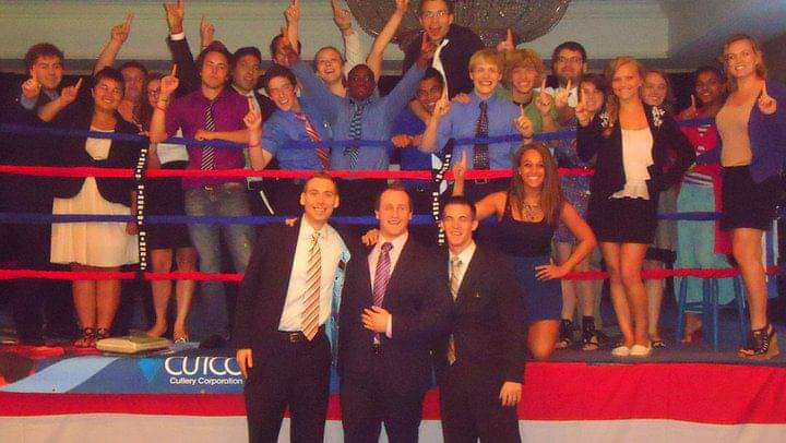 Group of people on stage, some raising hands, with three men in front holding an award or certificate.
