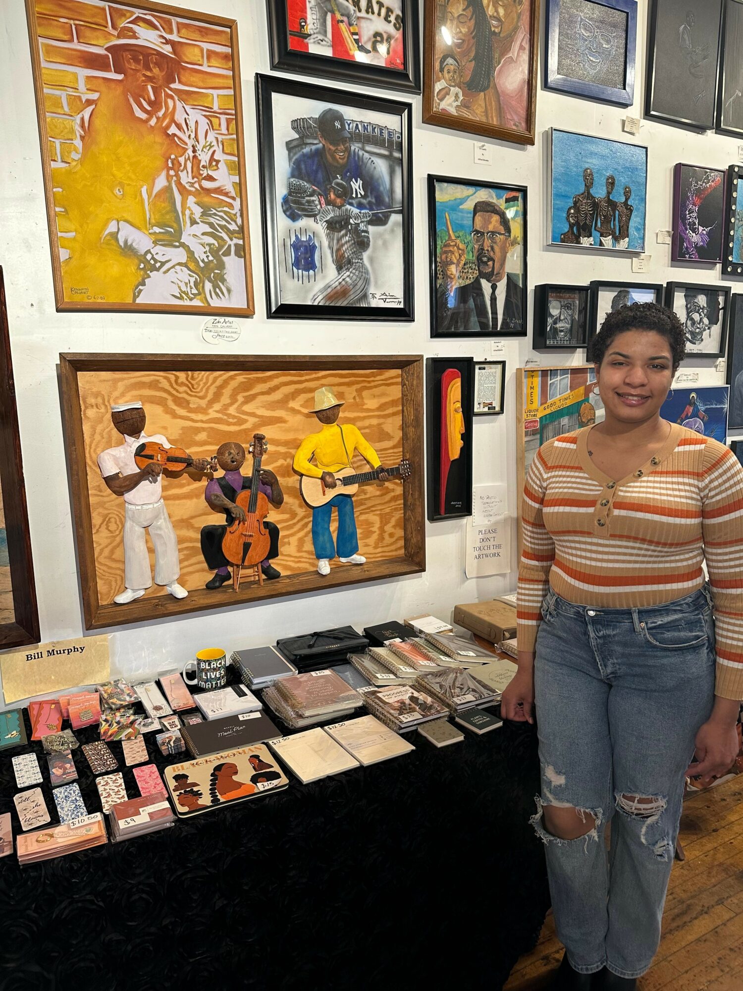 Young woman standing next to a table with various items, in an art gallery with framed artwork on the wall.
