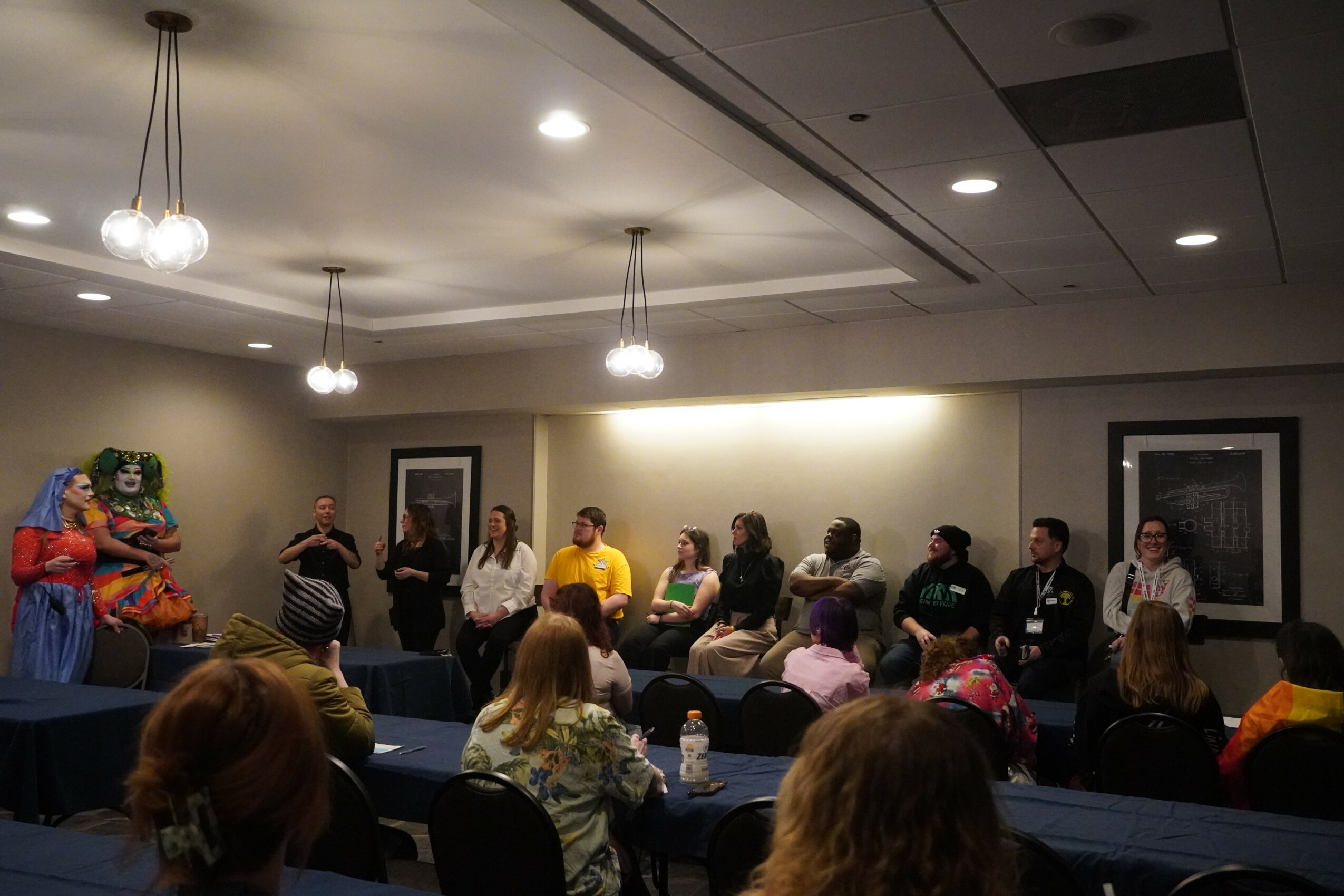 Panel of people seated at a long table in a room with hanging lights and framed pictures on the wall.