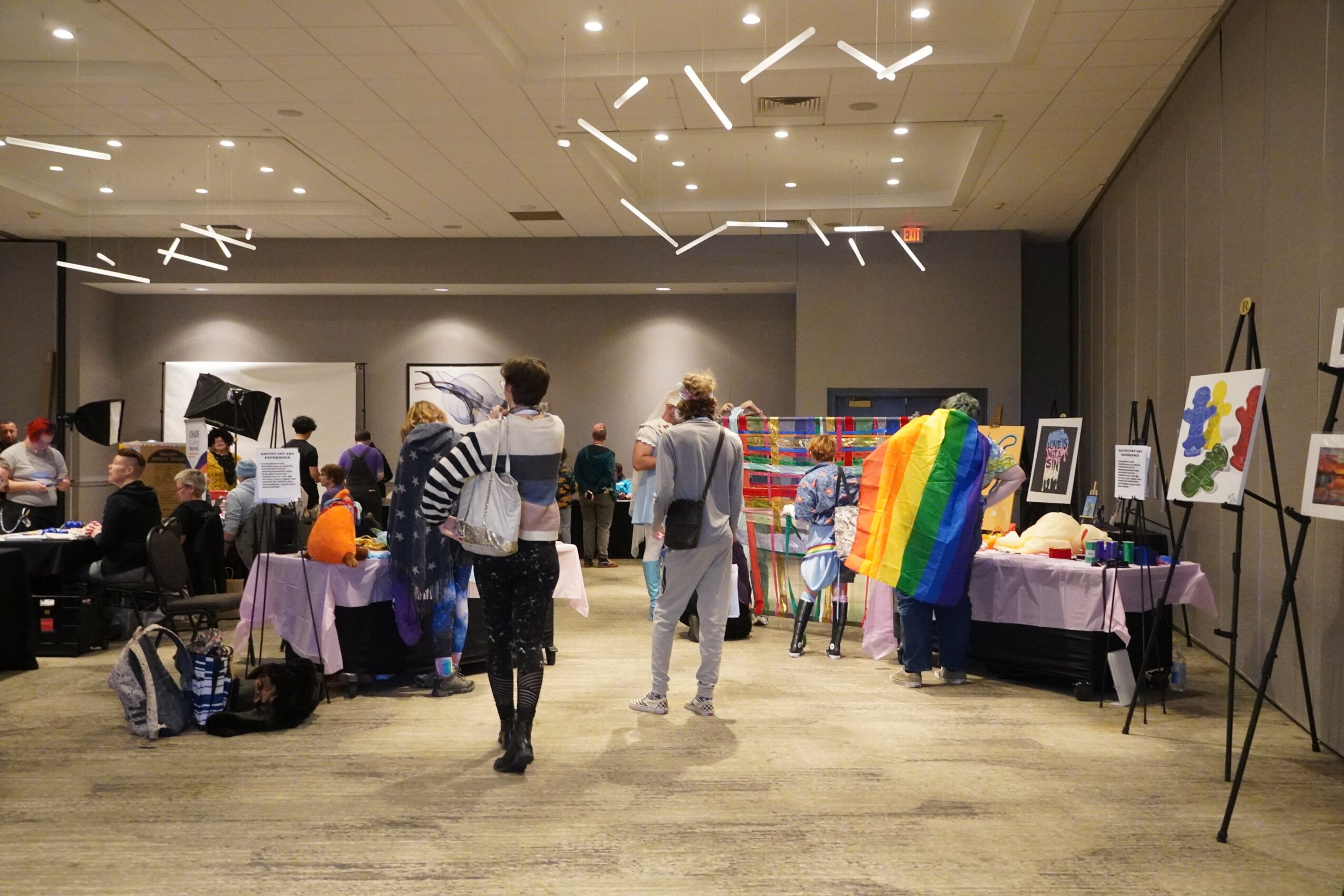 Indoor event with people, tables, artwork, and rainbow-colored decorations on display.