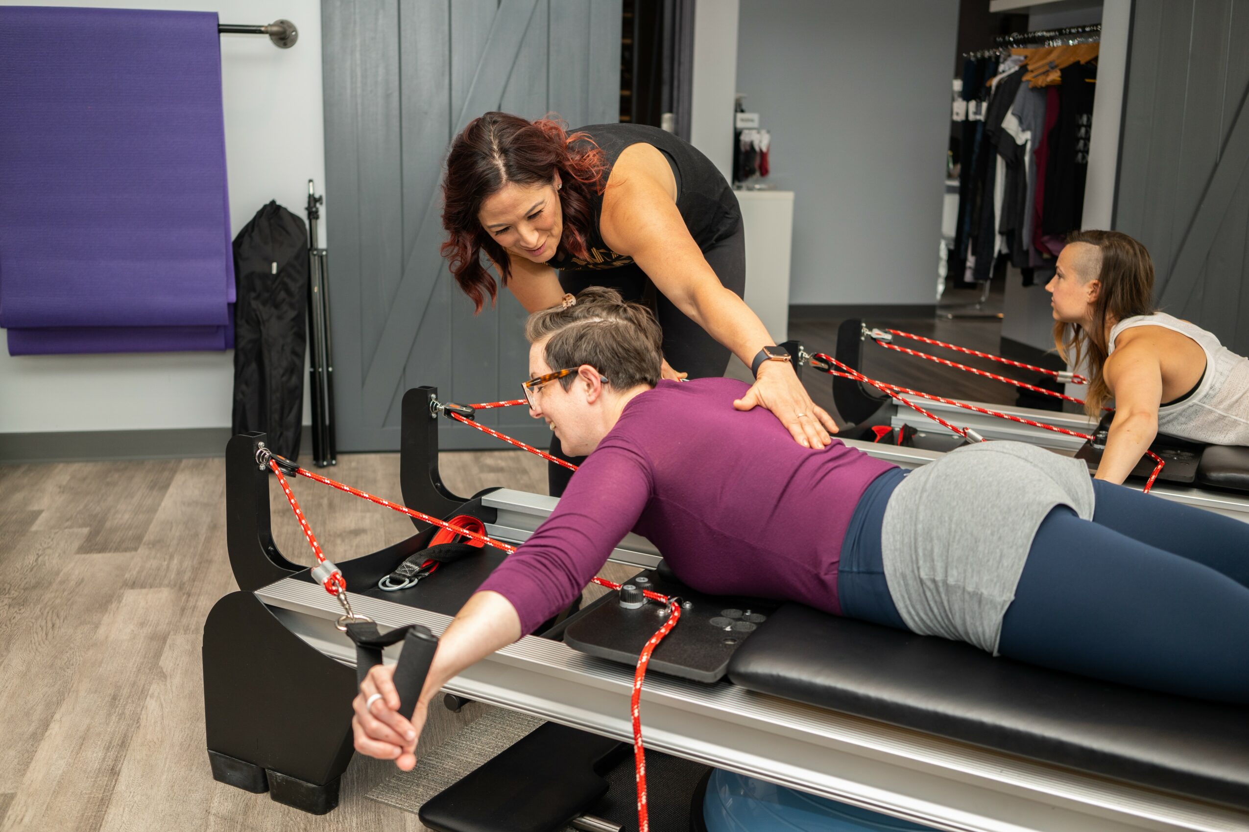 Woman lying on a black therapy table with a therapist assisting her, in a clinical setting with other people in background.