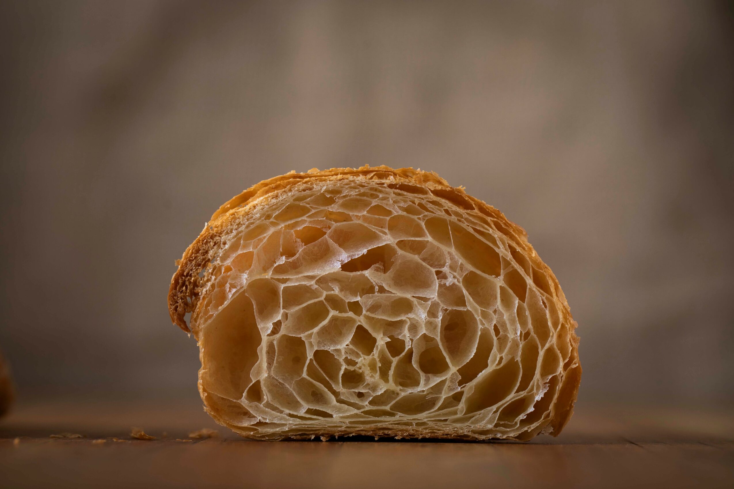 Close-up of a bread roll with a textured, airy interior on a wooden surface.