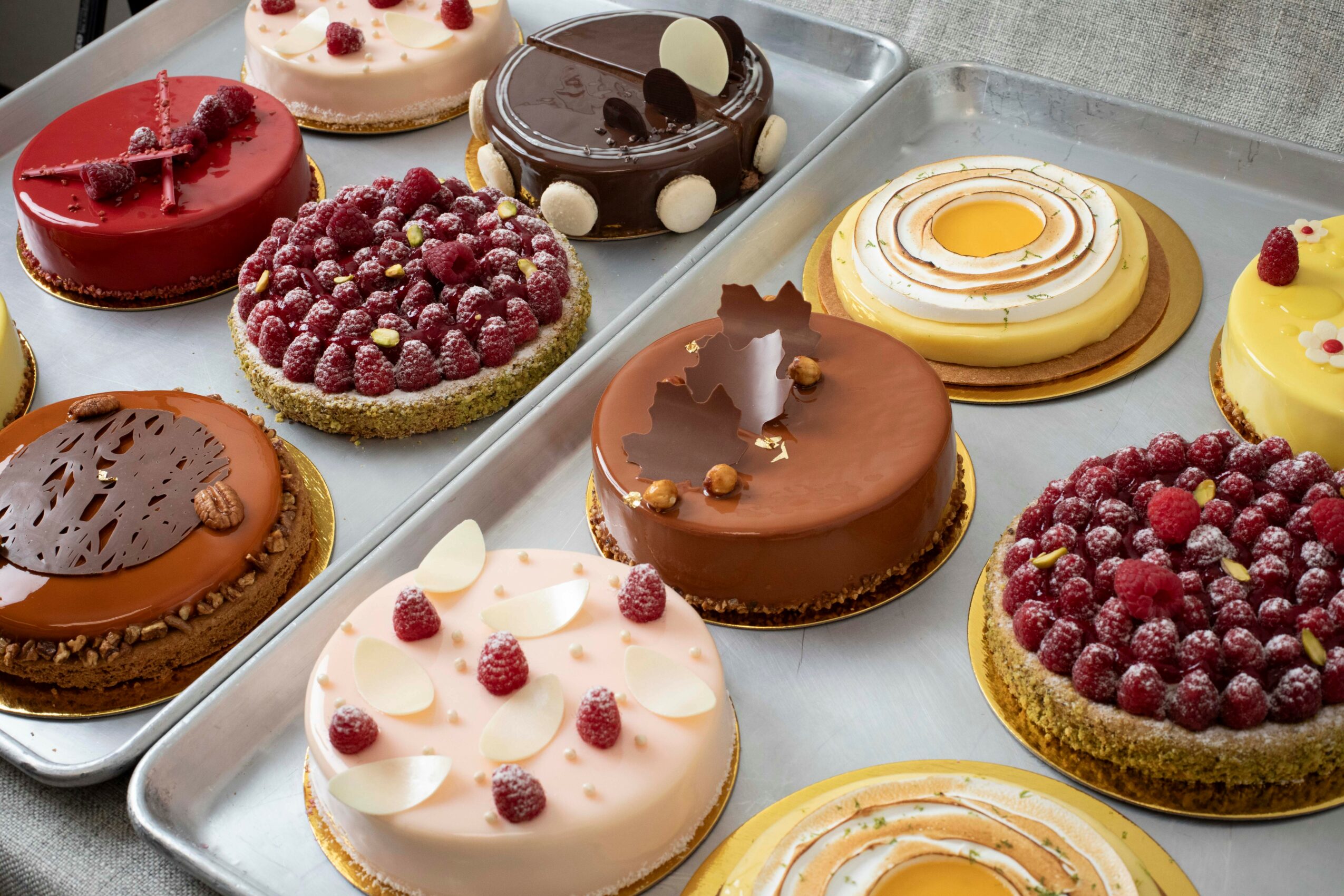 Assorted decorated cakes and pastries on a tray, including fruit-topped, chocolate, and cream-filled desserts.
