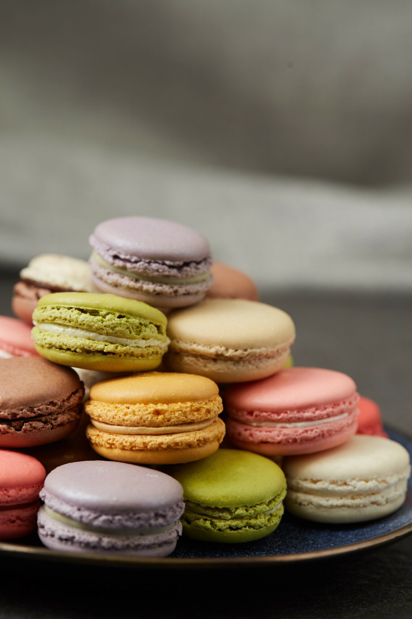 Assorted colorful macarons stacked on a plate with a blurred background.