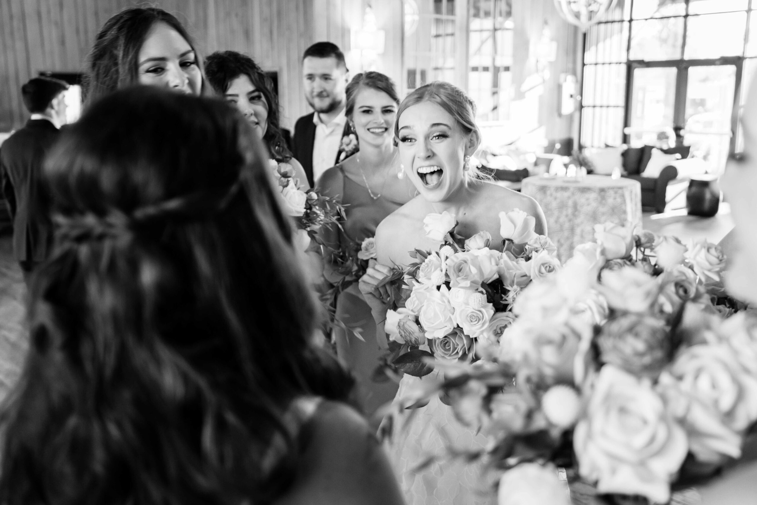 Group of women smiling and laughing, with a woman holding a bouquet of flowers in a bright room.
