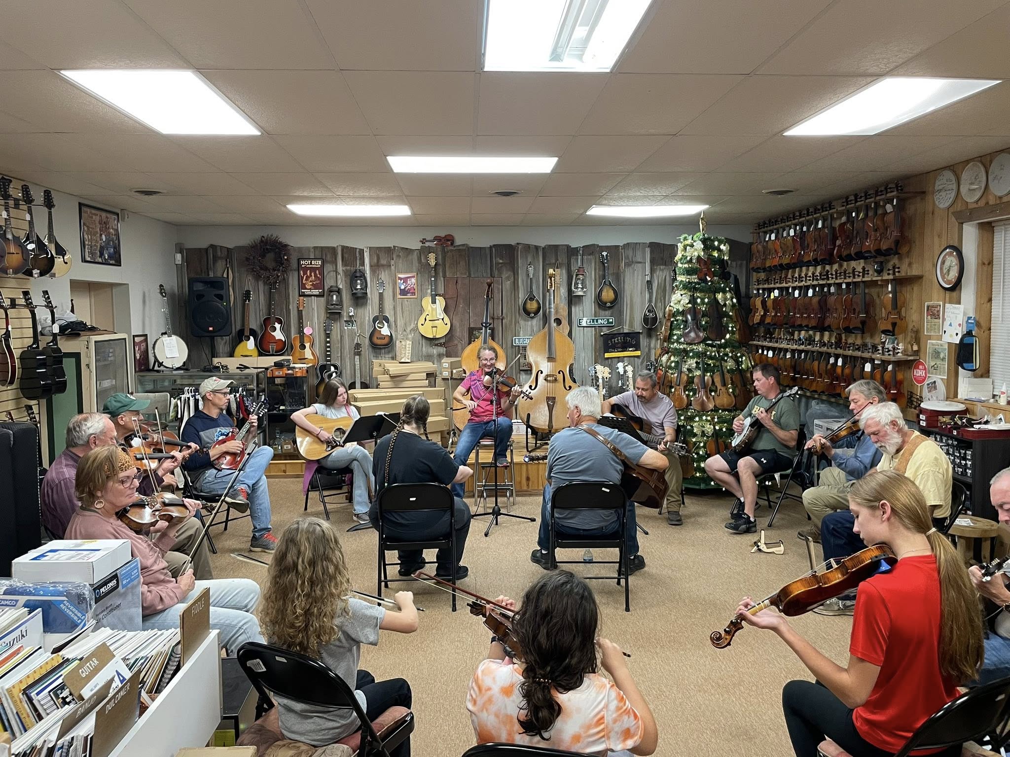 Group of people playing musical instruments in a room with shelves and decorations on the wall.