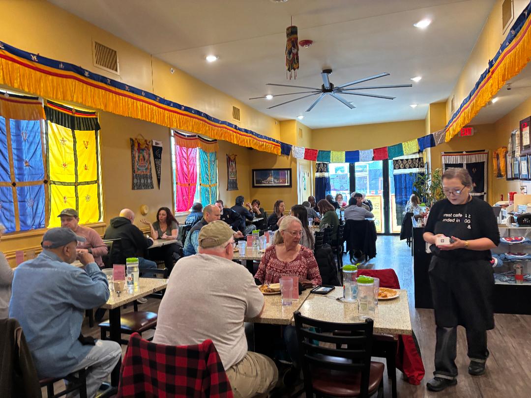 People sitting at tables in a colorful restaurant with yellow, pink, and blue curtains, and a person serving food.