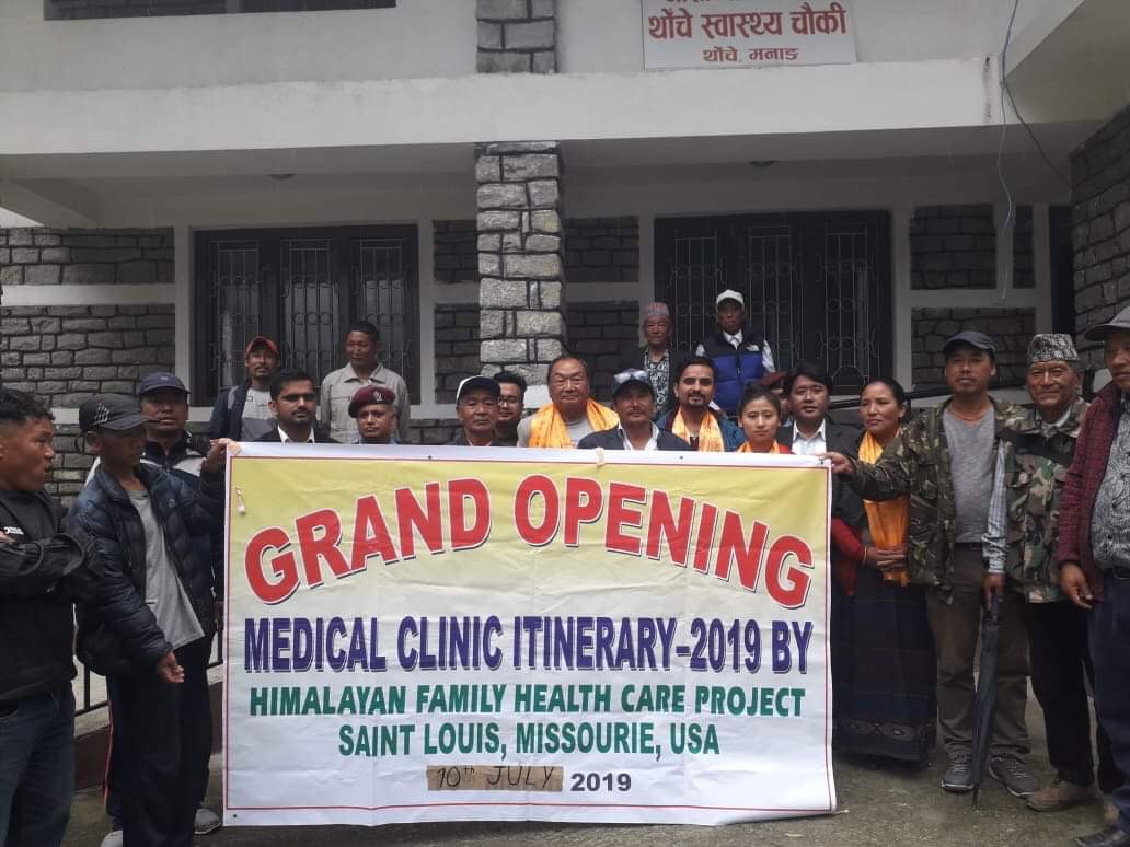 Group of people holding a banner outside a building for grand opening event in 2019.