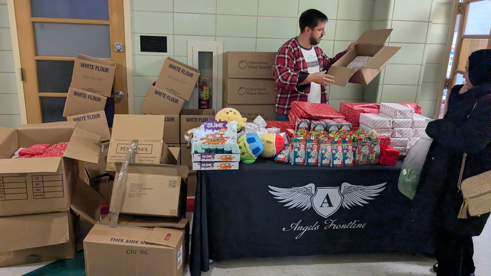 Person organizing boxes and supplies at a table with a black cloth, surrounded by cardboard boxes and packaged items.