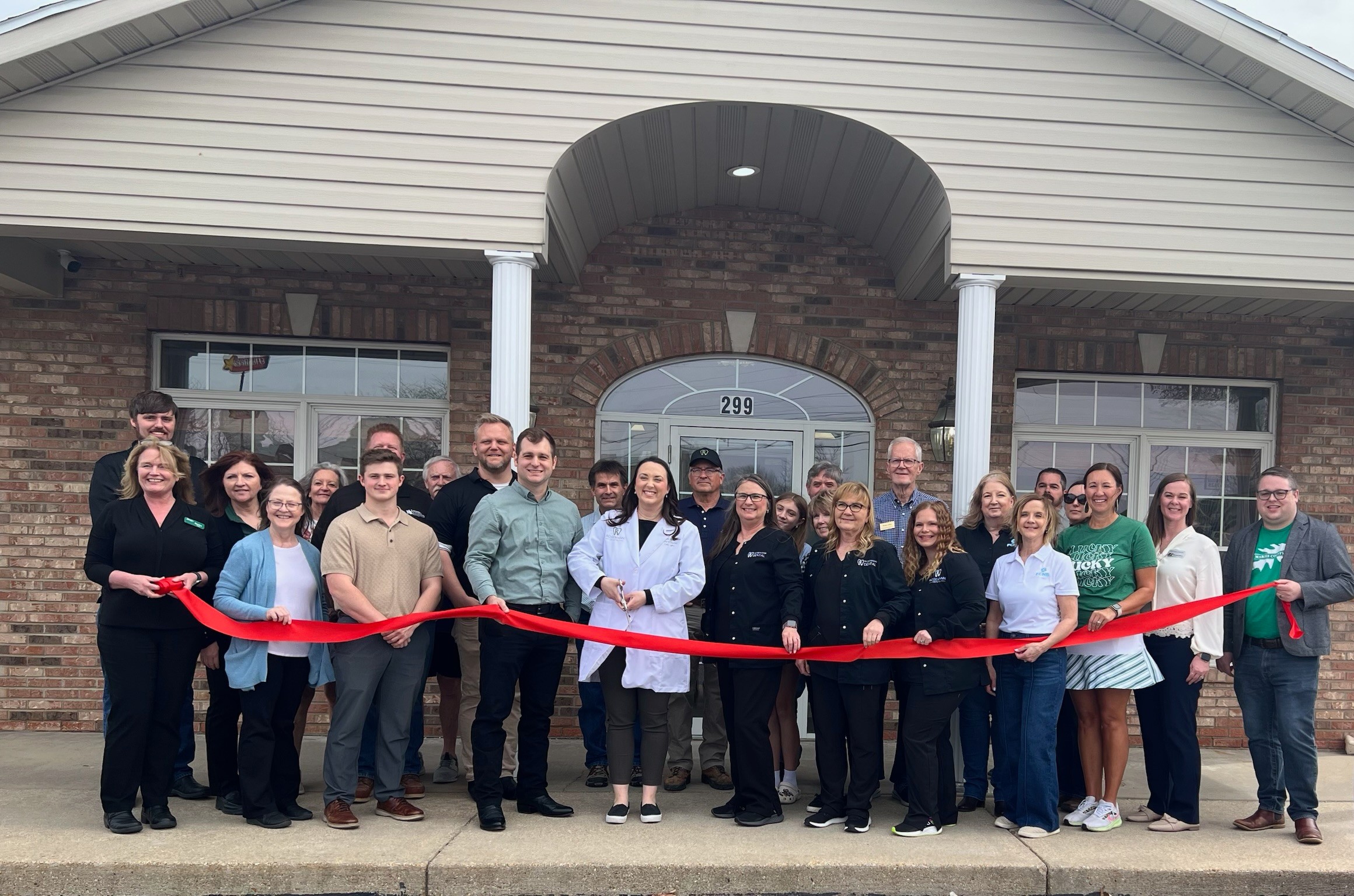 Group of people gathered outside a building for a ribbon-cutting ceremony, holding a red ribbon.