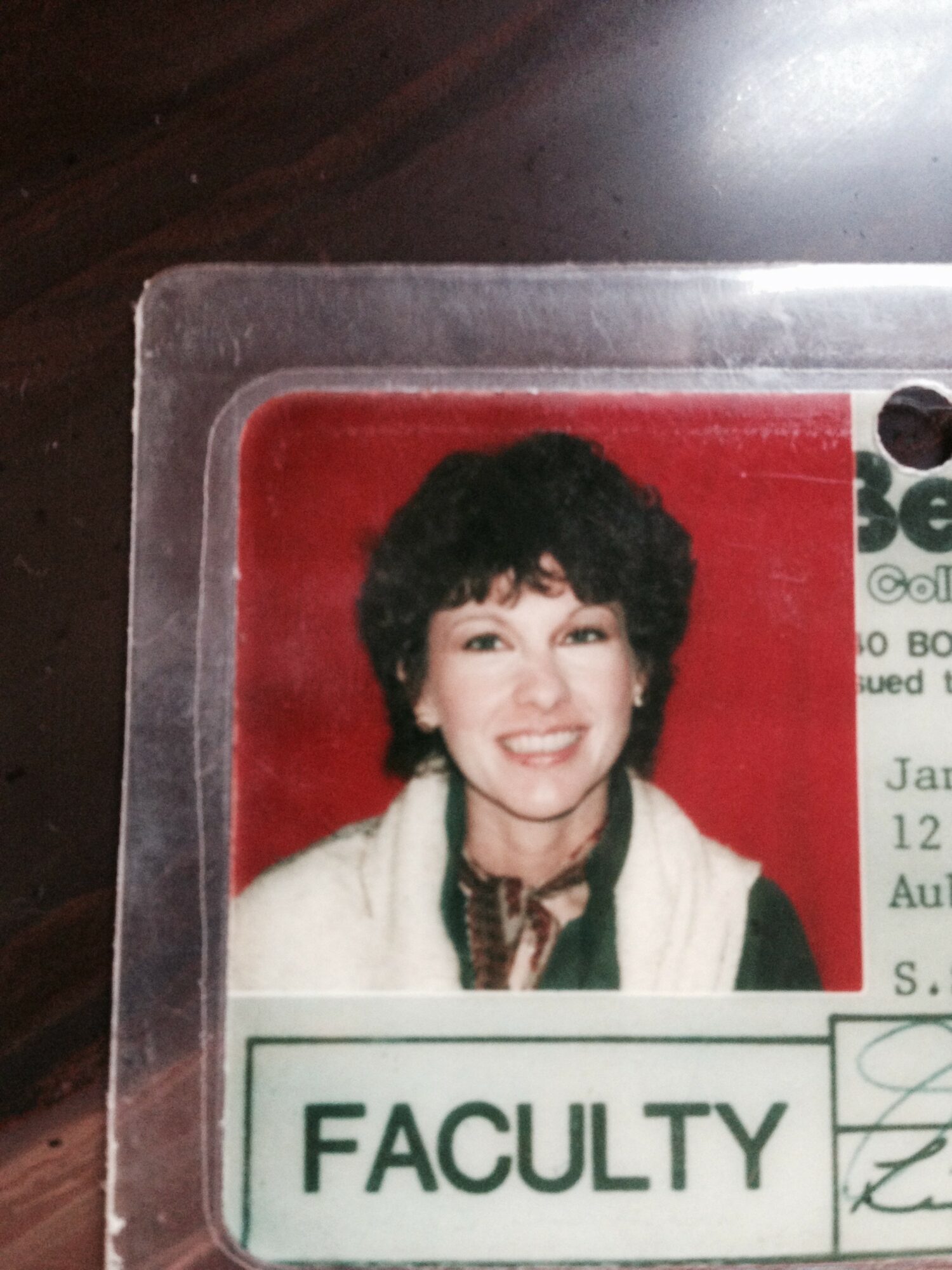 Photograph of a woman with short curly hair, smiling, wearing a white jacket and a scarf, labeled 'FACULTY'.