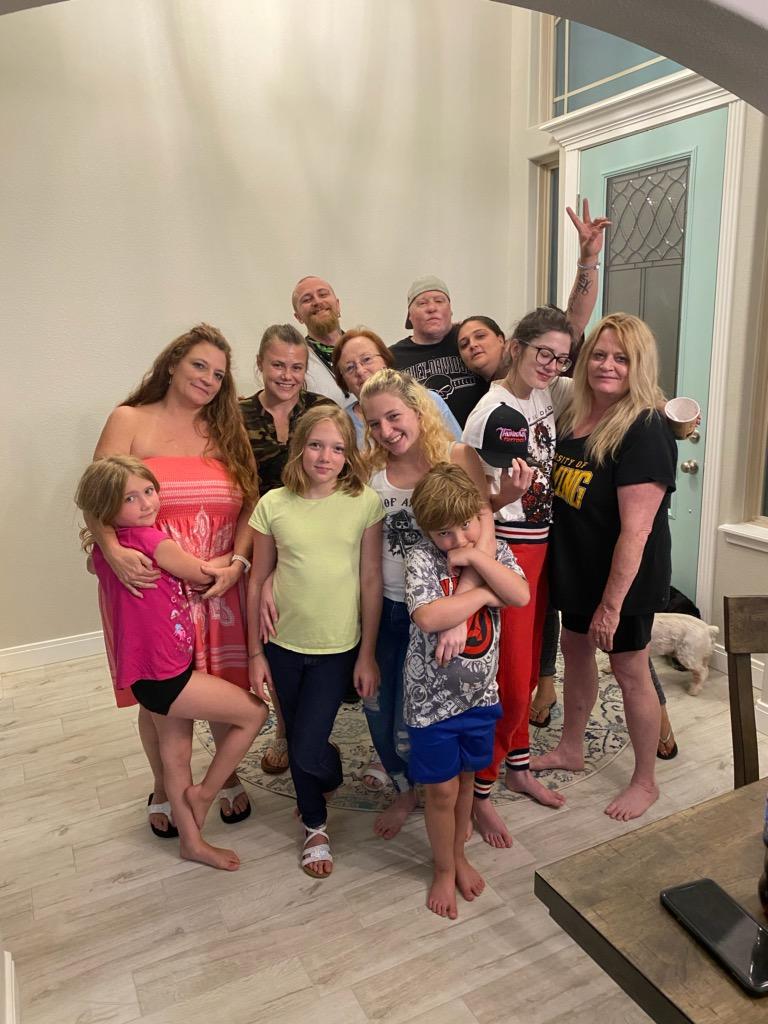 Group of children and adults posing indoors, some making peace signs, in a well-lit room with light-colored walls and a window.