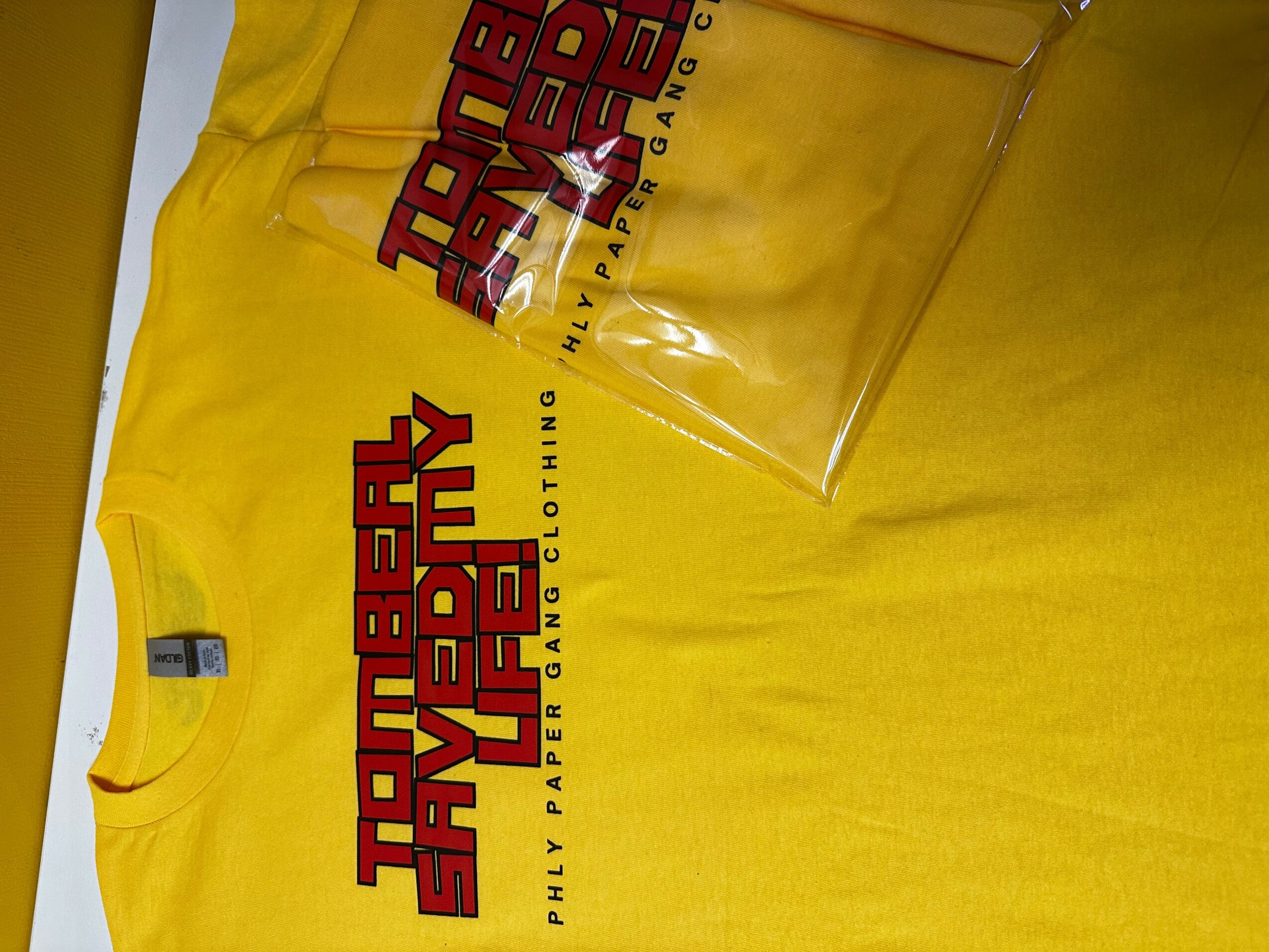Yellow T-shirt with red and black text, partially visible, on a yellow background, with a clear glass nearby.