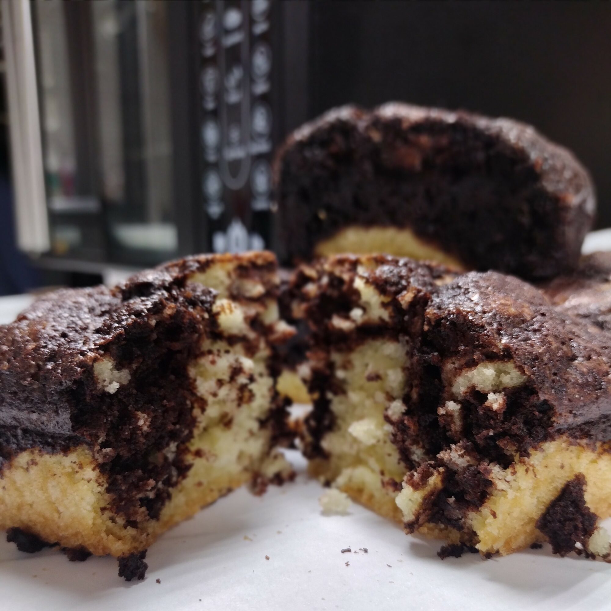 Chocolate marble cake with a moist interior, partially sliced, on a white surface with a dark background.