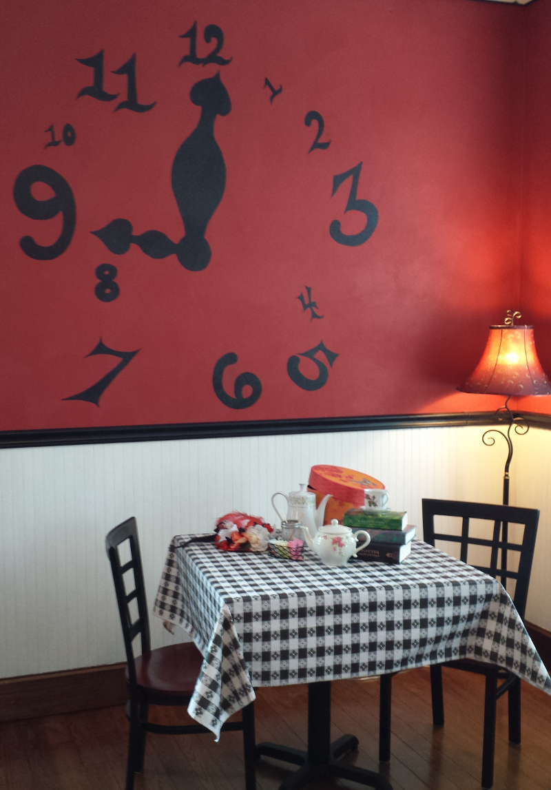 Dining table with checkered tablecloth, teapot, and chairs in a room with a red wall and large clock design.