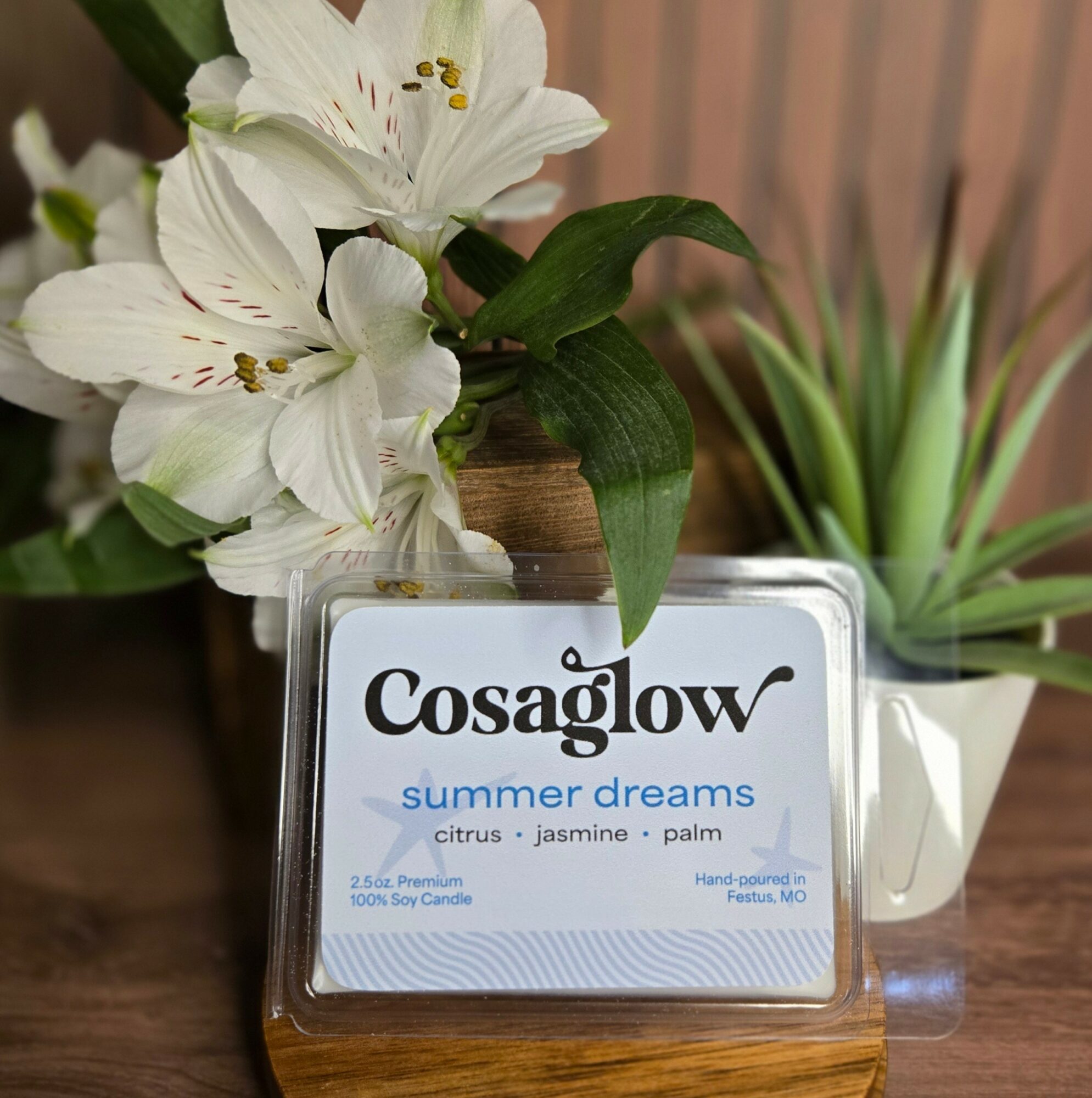 A scented candle labeled 'Cosaglow summer dreams' with floral and plant decorations in the background.