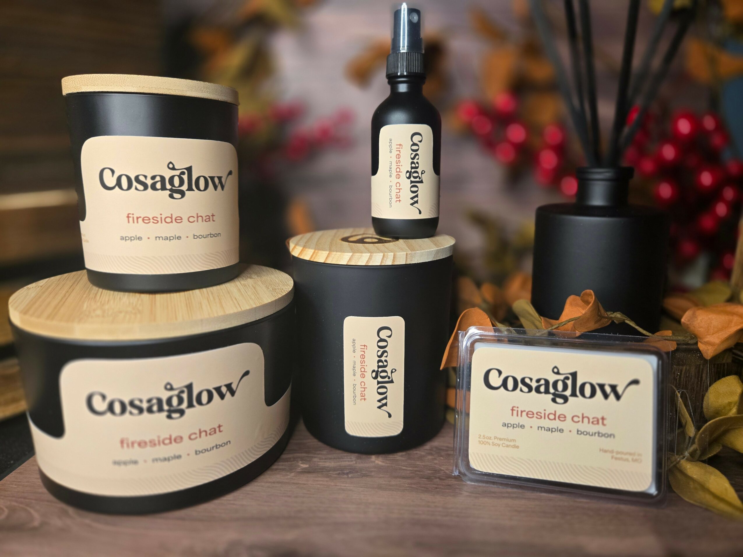 Collection of Cosaglow fireside chat products including candles, diffuser, and spray on a wooden surface with autumn decorations.