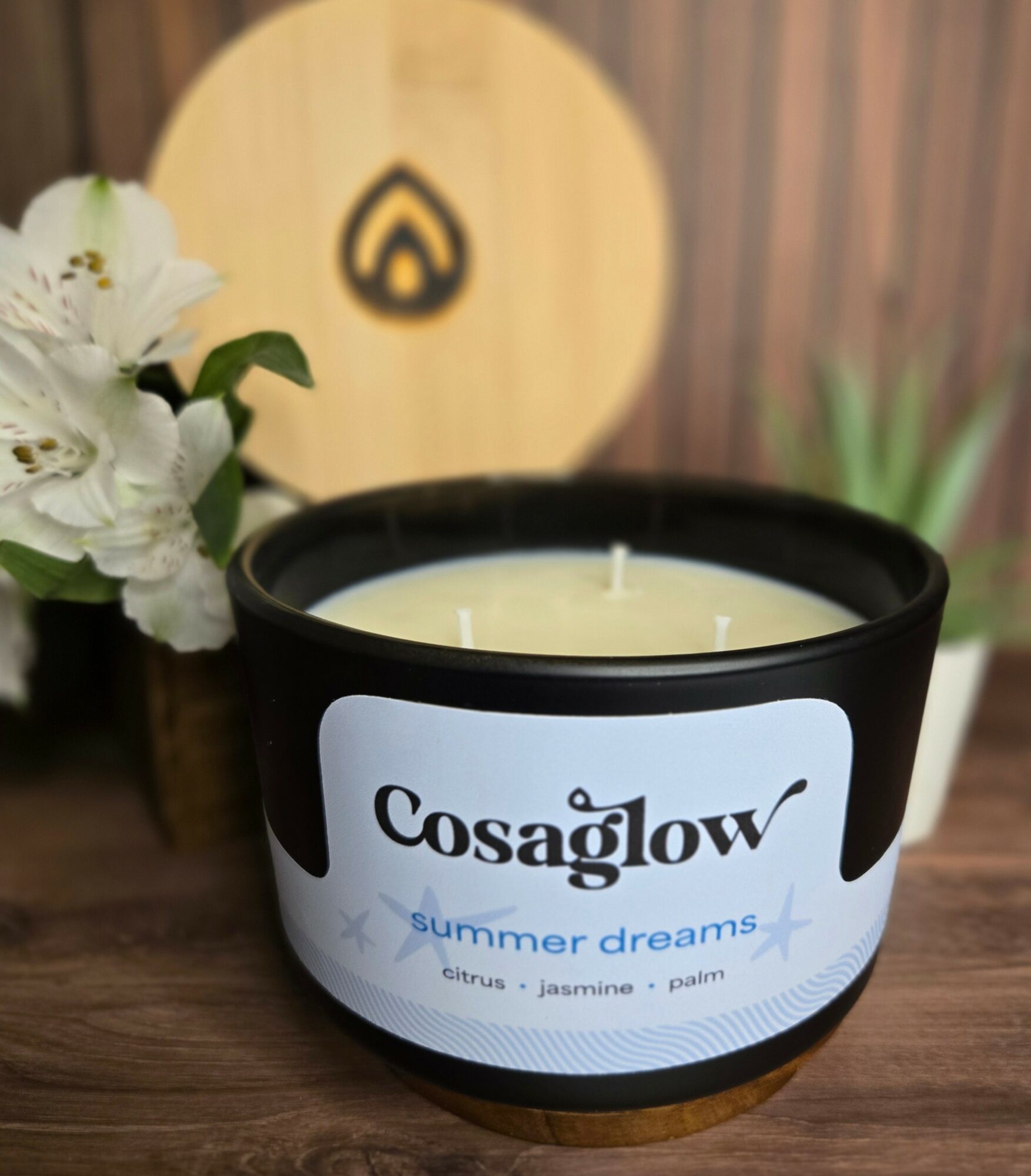 A black candle holder with a white label reading 'Cosaglow summer dreams' and a candle inside, placed on a wooden surface.