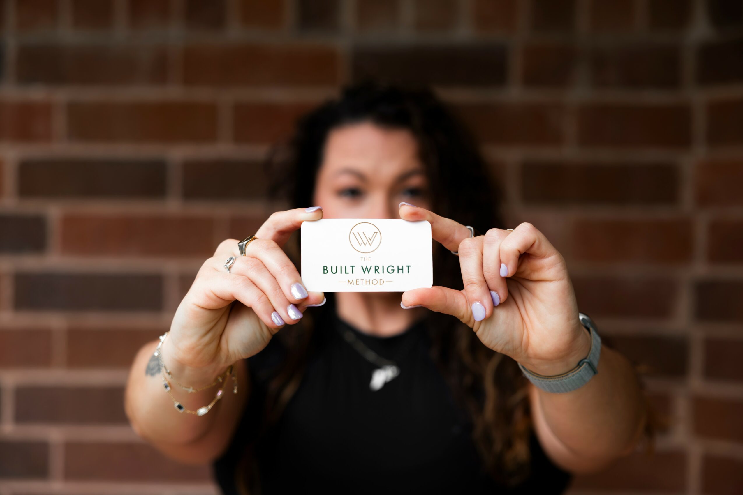 Person holding a business card with the name 'Built Wright' in front of a brick wall, face partially obscured.
