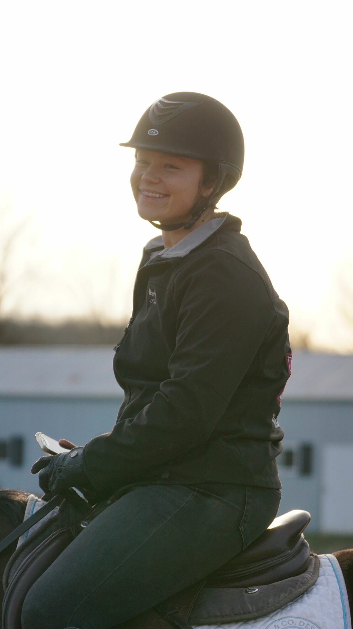 Person wearing a helmet and jacket, sitting outdoors with a neutral expression, facing sideways, with a blurred background.
