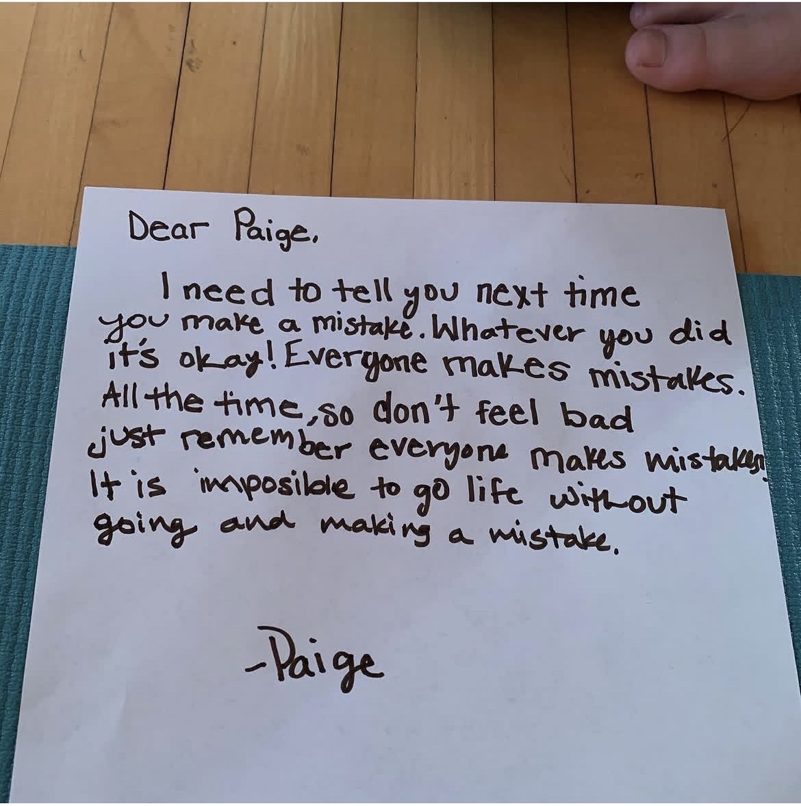 Handwritten note on paper with a wooden surface background, addressed to Paige, offering reassurance and encouragement.
