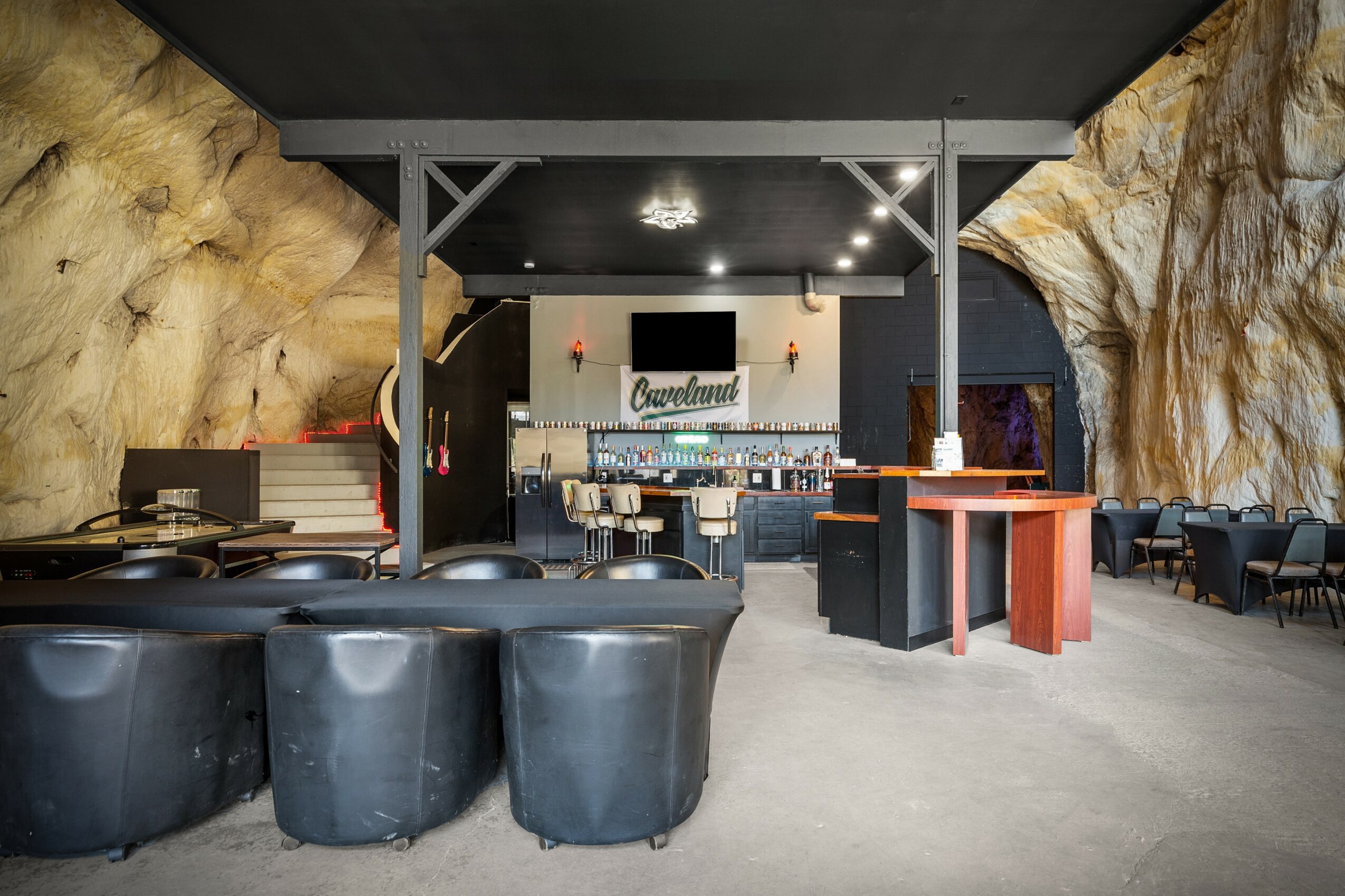 Interior of a cave-like venue with seating, a bar area, and a sign reading 'Cavehouse' in the background.