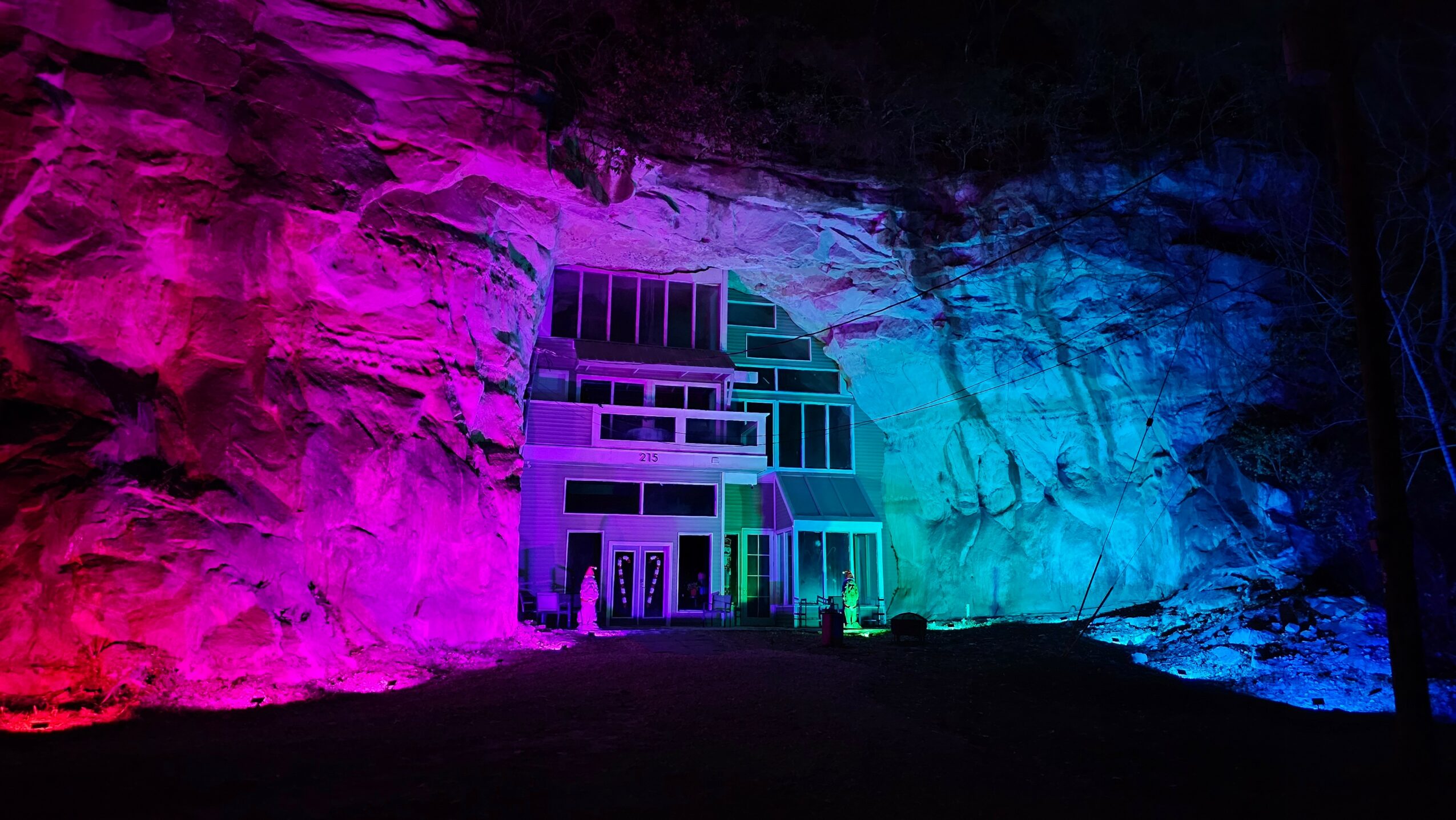 Colorful light display on a building and rocky wall, with pink, purple, blue, and green hues.