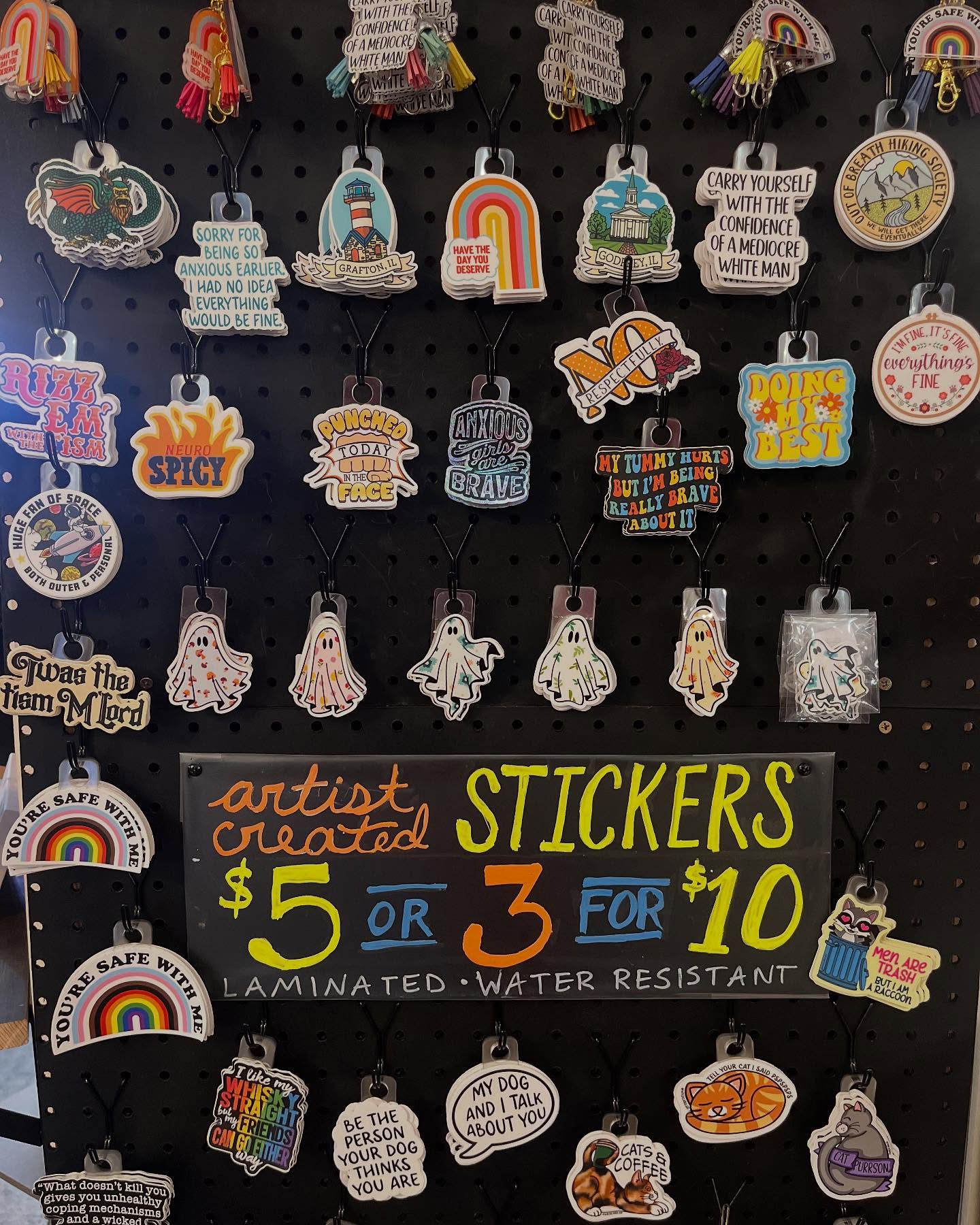 Display of various colorful stickers and a chalkboard sign with pricing and description, arranged on a dark background.