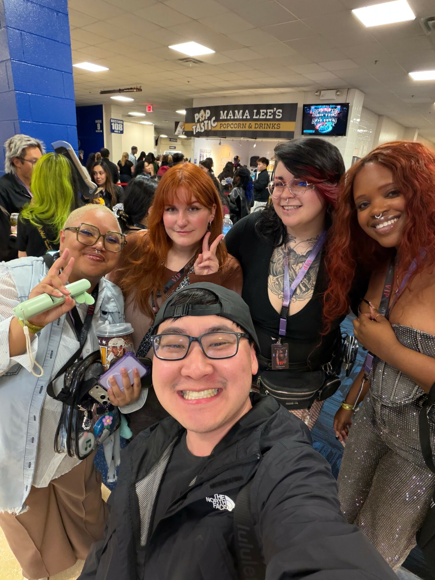 Group of five people smiling and posing for a photo indoors, with a crowd and a sign reading 'Mama Lees' in the background.