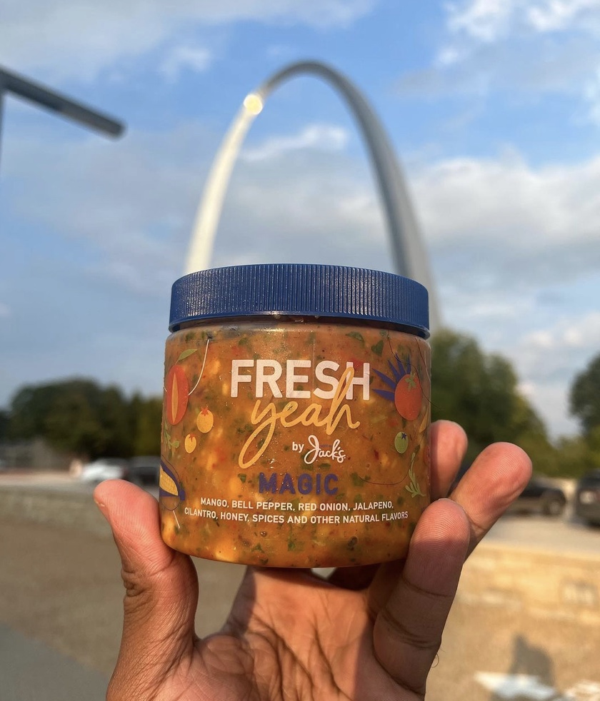 Hand holding a jar labeled 'FRESH yeah' with a cityscape and the Gateway Arch in the background.