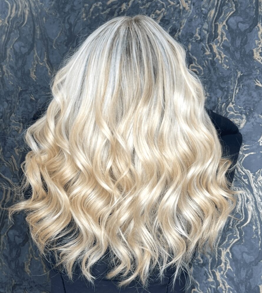 Back of a person with long, wavy, platinum blonde hair against a dark marbled background.
