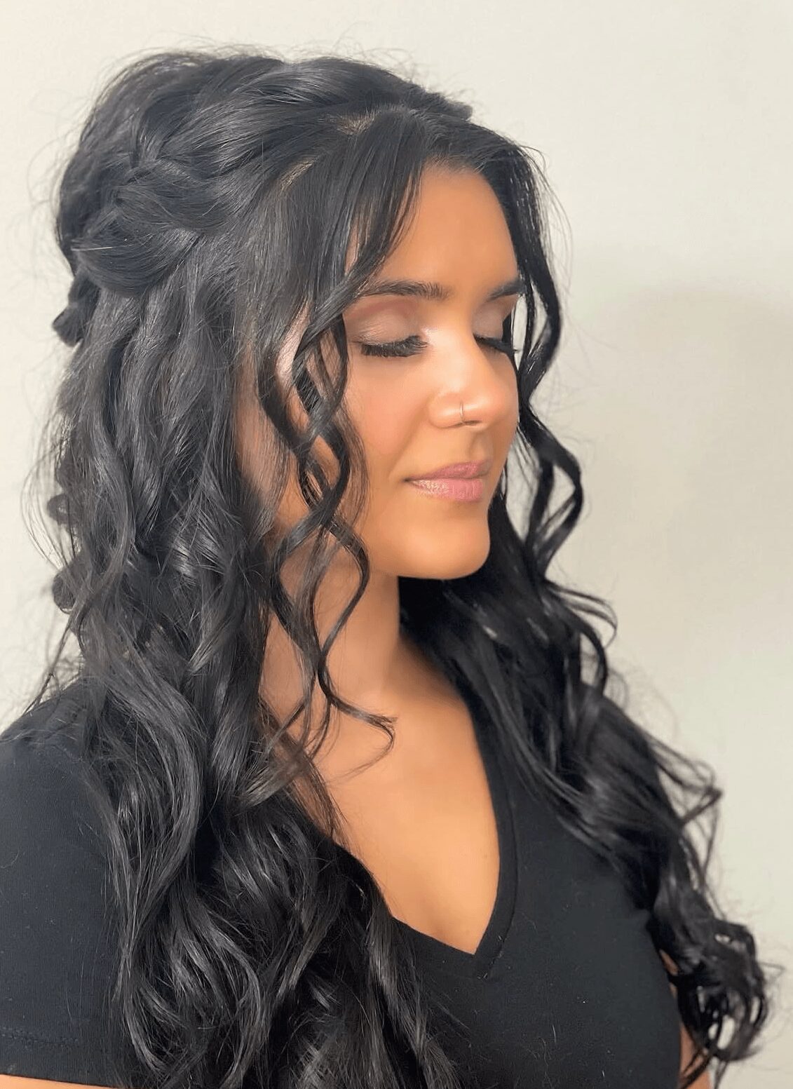 Woman with long, curly dark hair and closed eyes, wearing a black top, facing right.