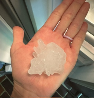 Hand holding a large piece of ice, with a window and indoor setting in background.