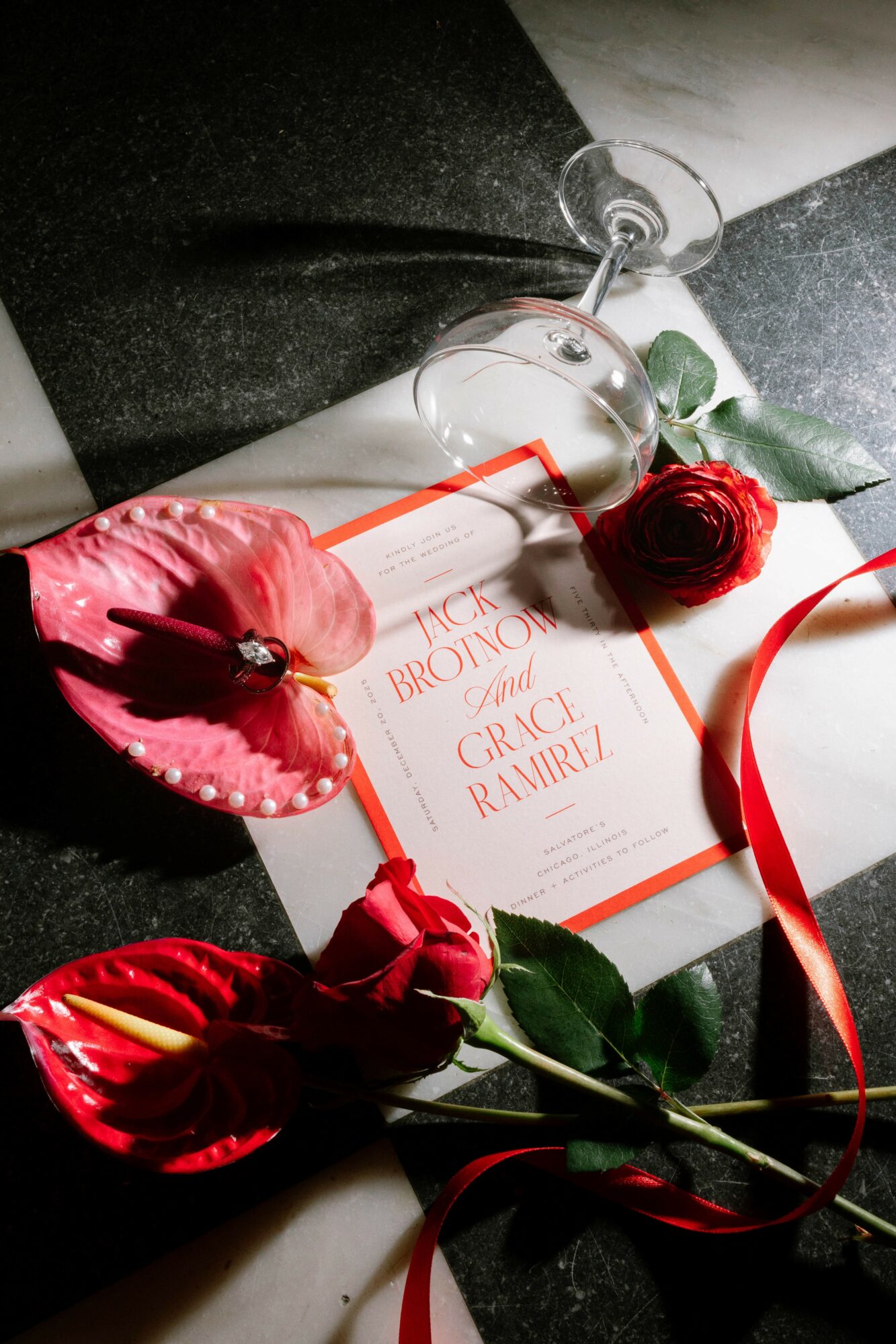A glass bottle, red roses, and a book with a red cover on a dark surface, with a white background.