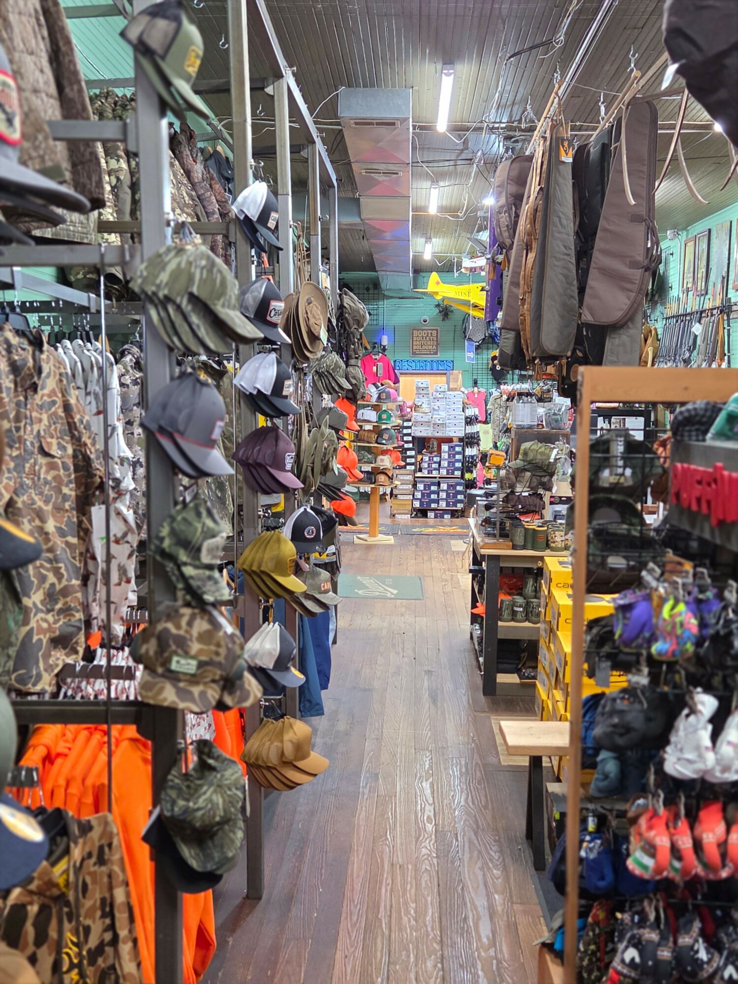 A narrow aisle in a store with clothing, hats, and accessories on shelves and racks, extending into the background.