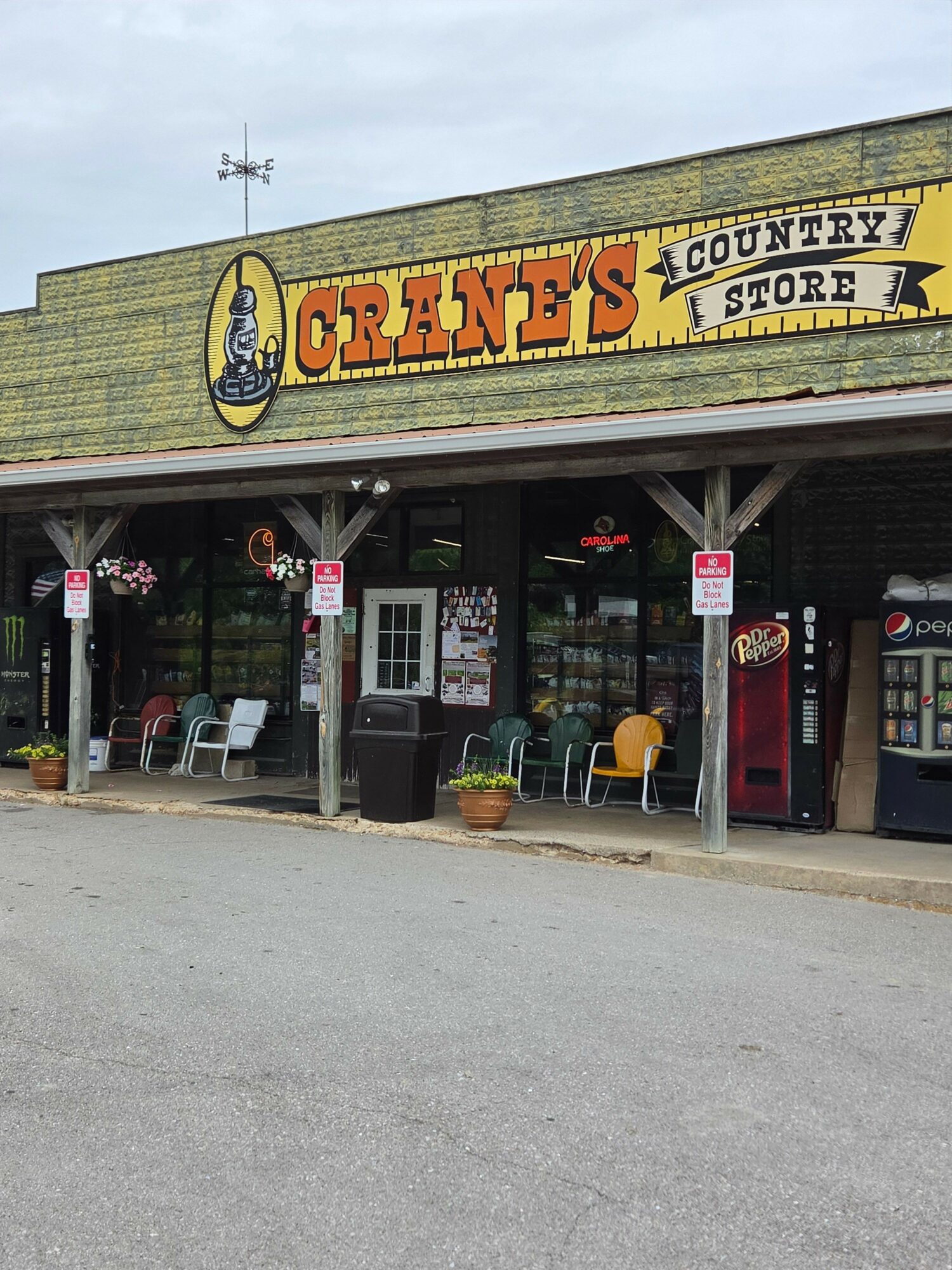 Storefront with a yellow sign reading 'CRANE'S COUNTRY STORE' and outdoor seating area with chairs and potted plants.