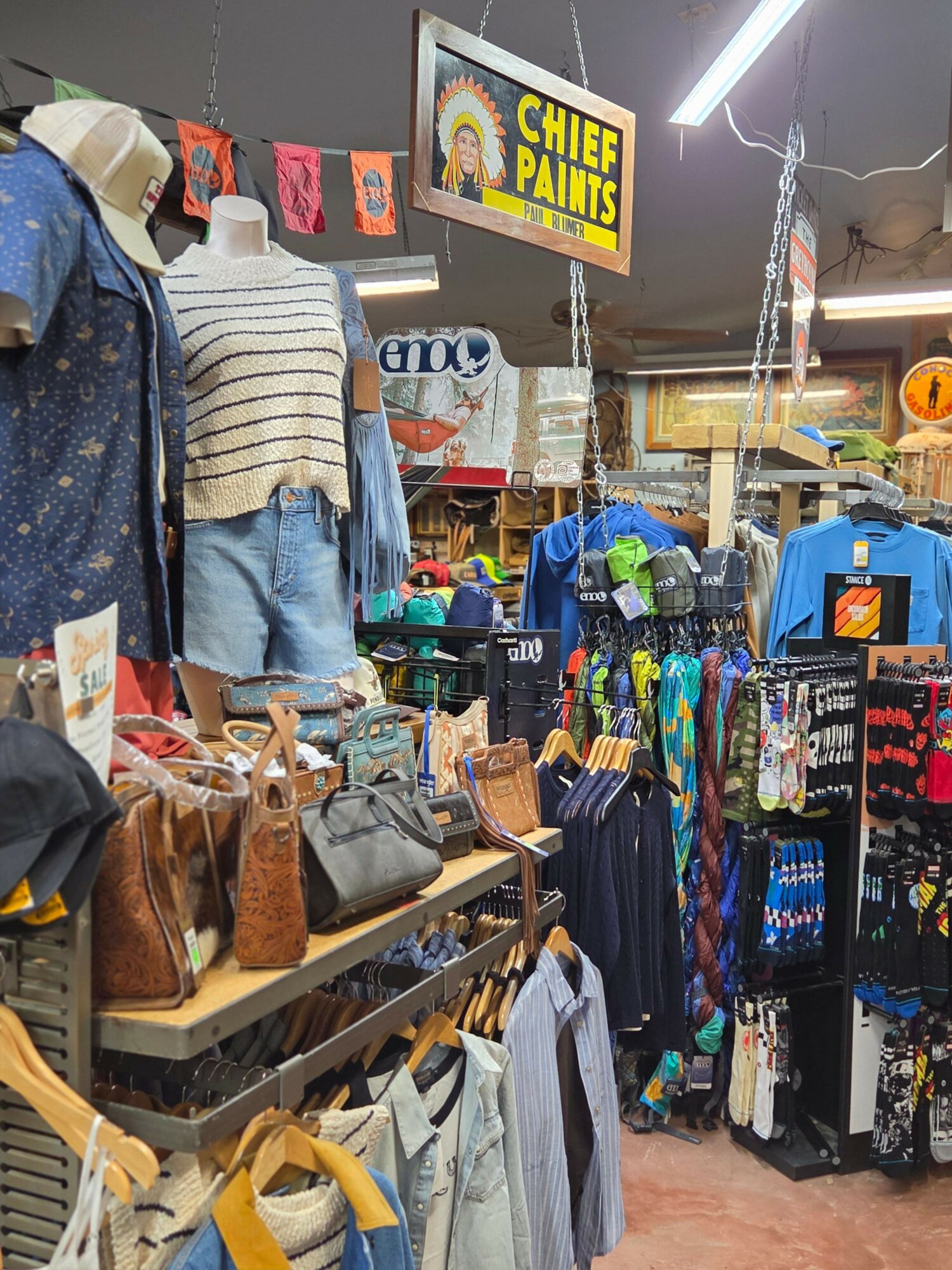 Clothing and accessories displayed at a market stall with a sign reading 'Chief Paints' in the background.