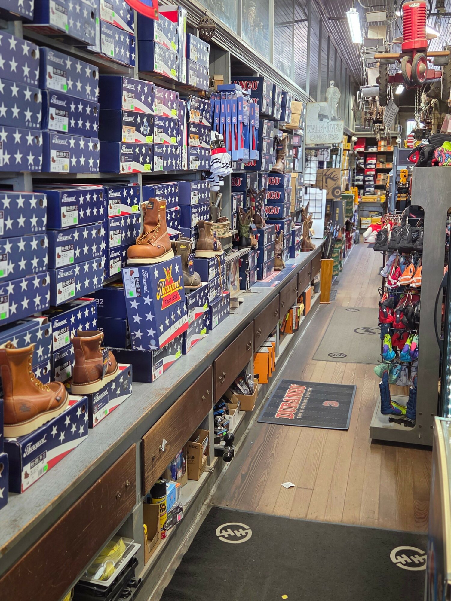 Store aisle with patriotic-themed items, including boots and boxes with stars and stripes, shelves on both sides, and a mat on the floor.