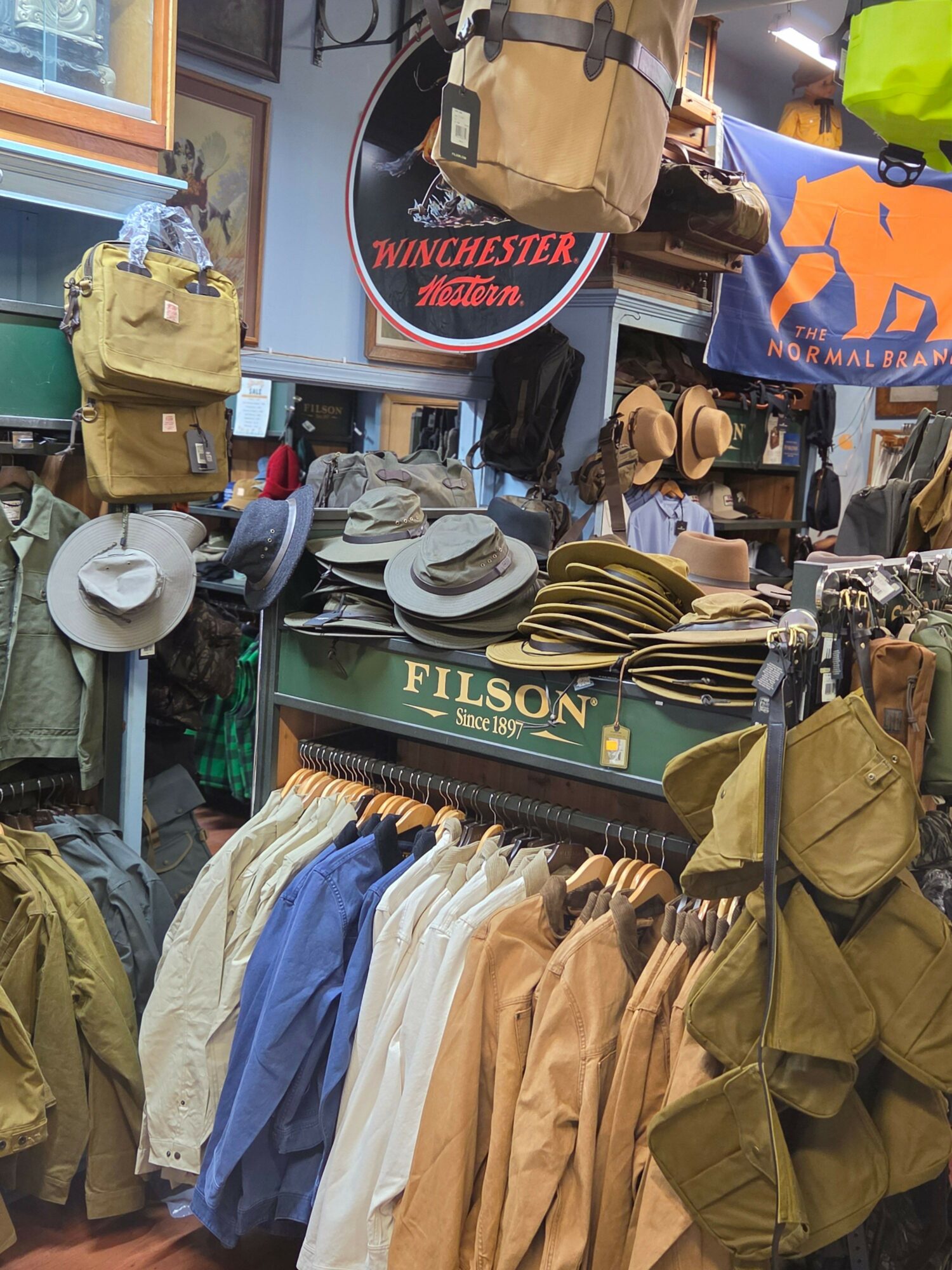 Display of hats, jackets, and bags in a store with signs and clothing racks visible in the background.