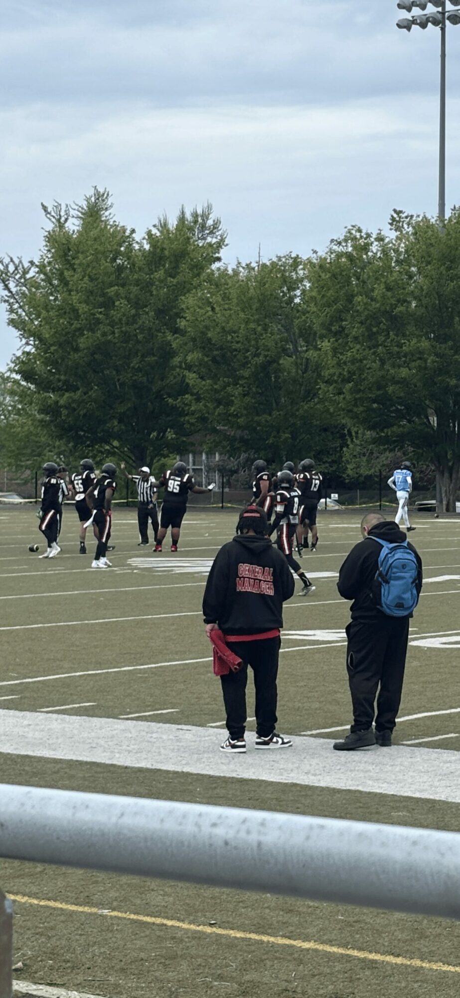 People standing on a sports field with trees and a cloudy sky in the background.
