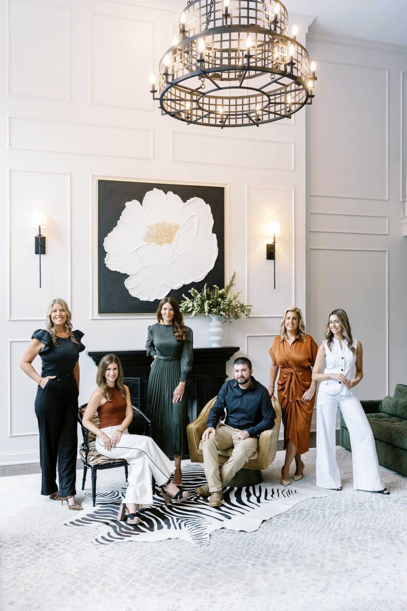 Group of six people in a bright, elegant room with a large floral artwork, chandelier, and modern decor.
