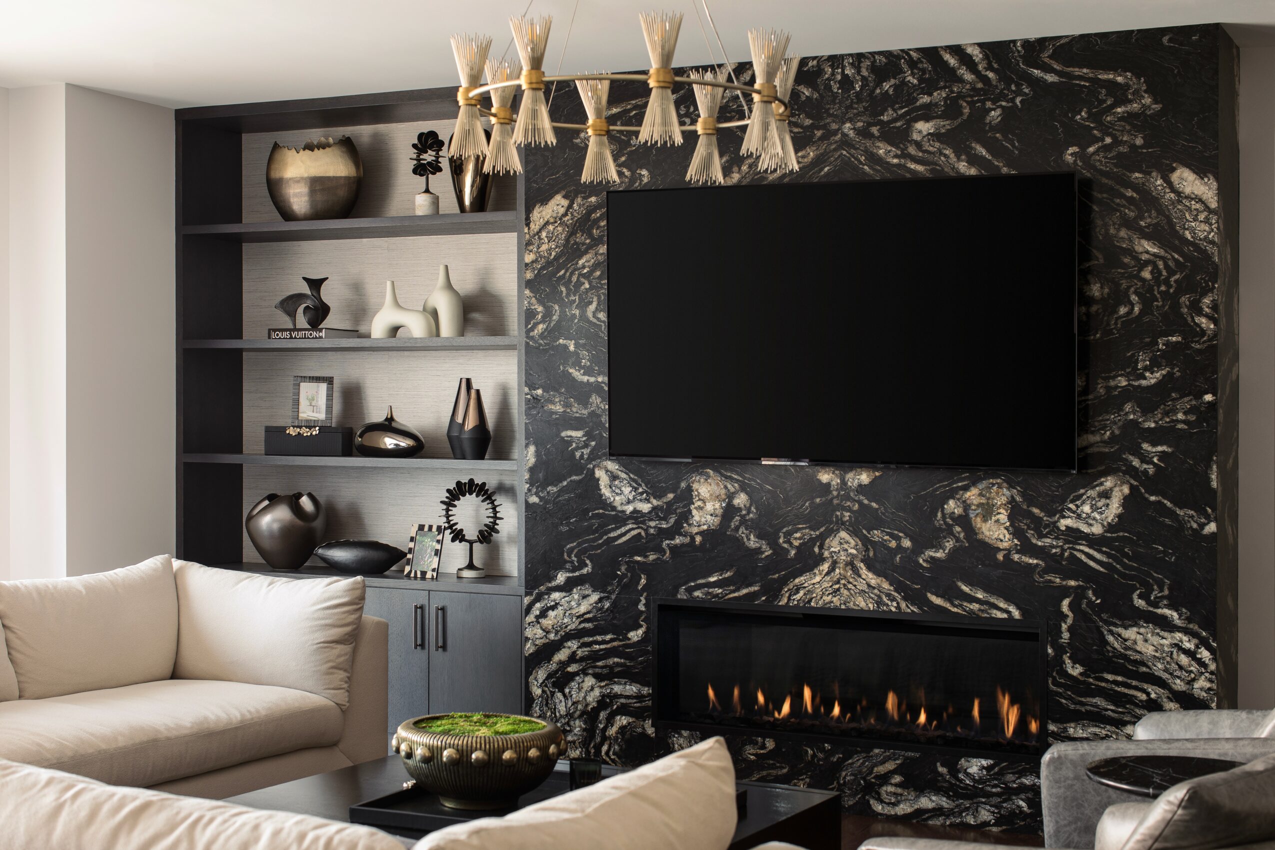 Living room with a beige sofa, black marble wall with a TV and fireplace, and a built-in shelf with decorative items.