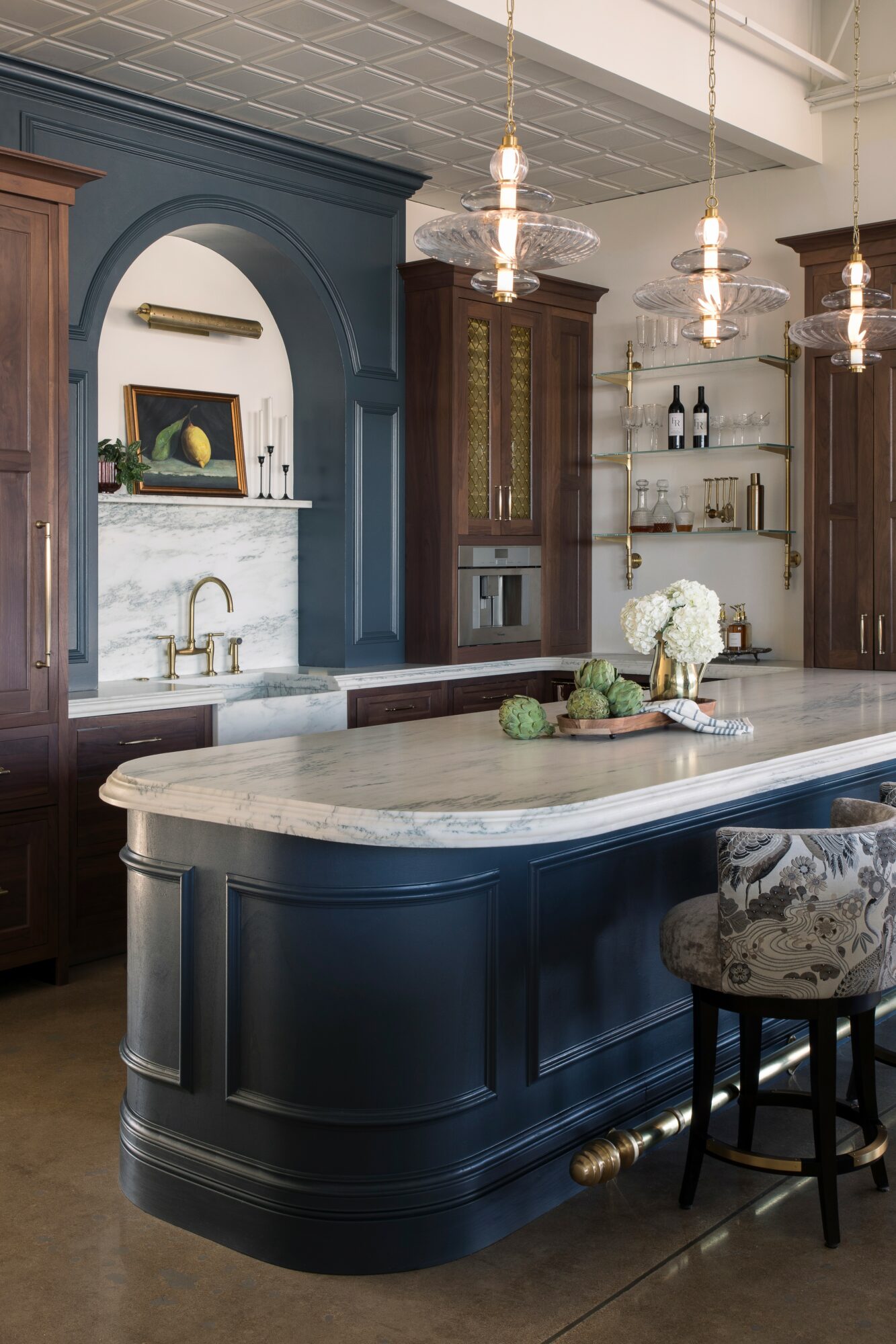 Kitchen with dark blue island, marble countertop, wooden cabinets, and pendant lights, featuring a decorative arch and open shelves.