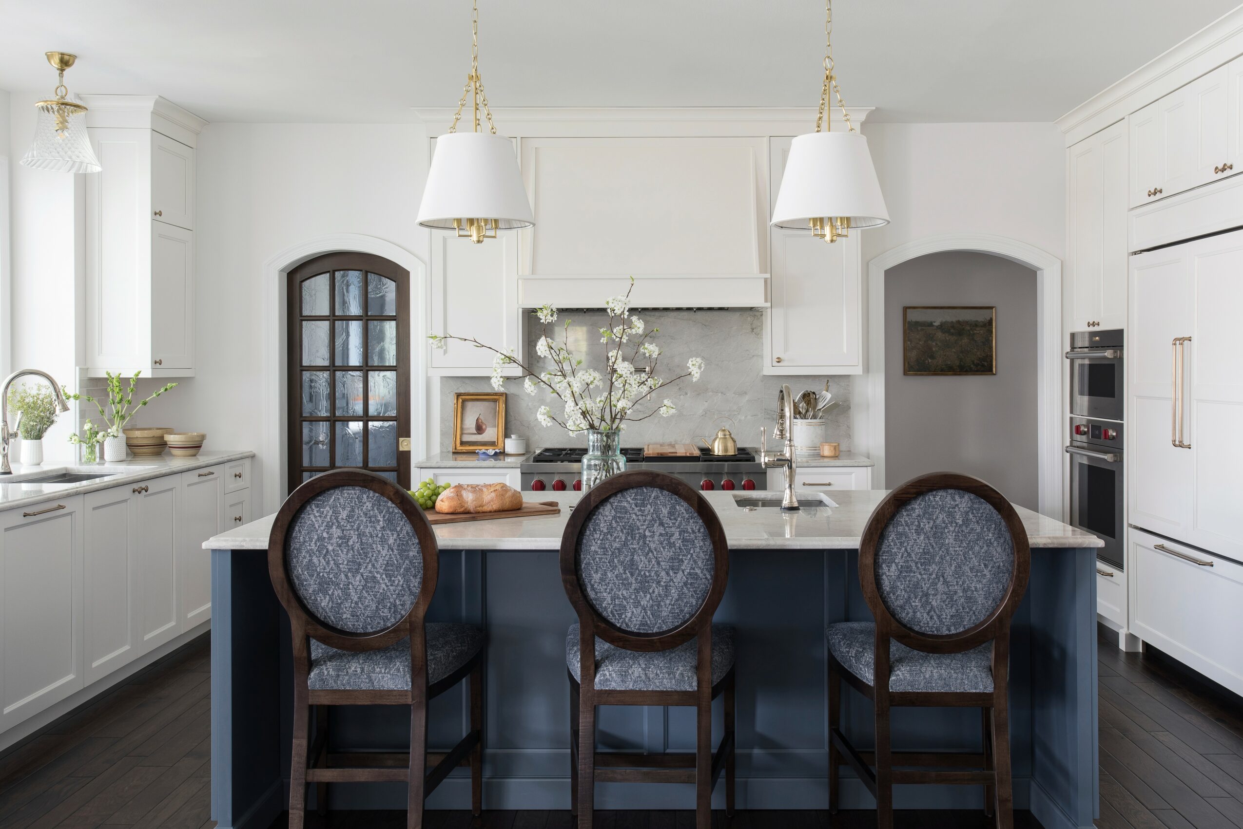 Bright kitchen with white cabinets, island with three chairs, and pendant lights, featuring a vase with flowers on the counter.