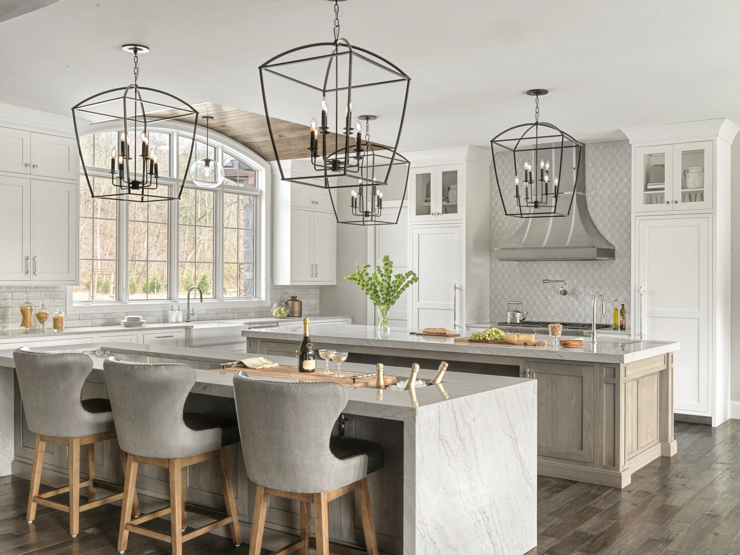 Modern kitchen with white cabinets, large window, island with seating, and black geometric pendant lights.