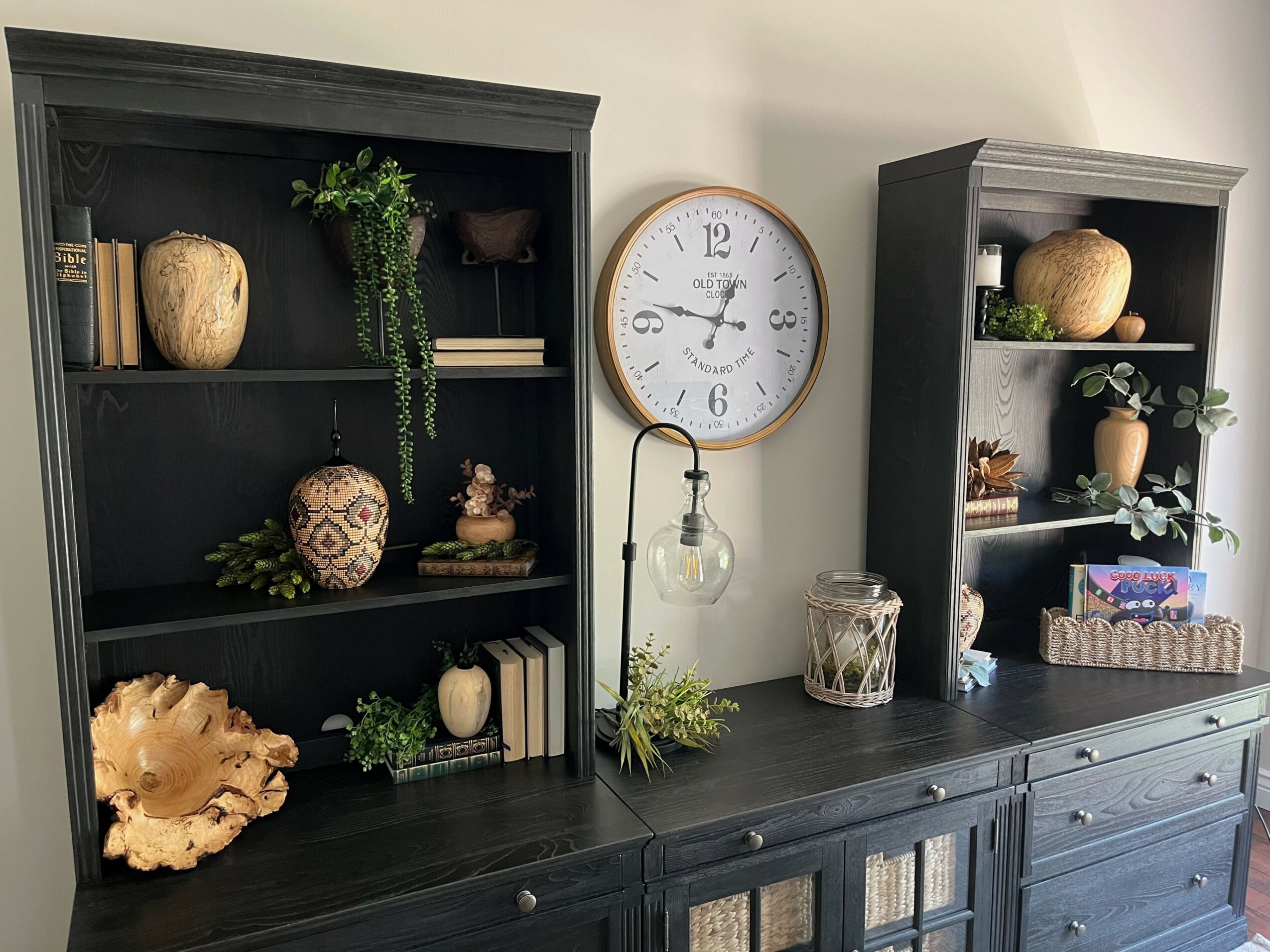 Decorative shelves with plants, vases, and books, a wall clock, and a dark wooden dresser with additional decor items.
