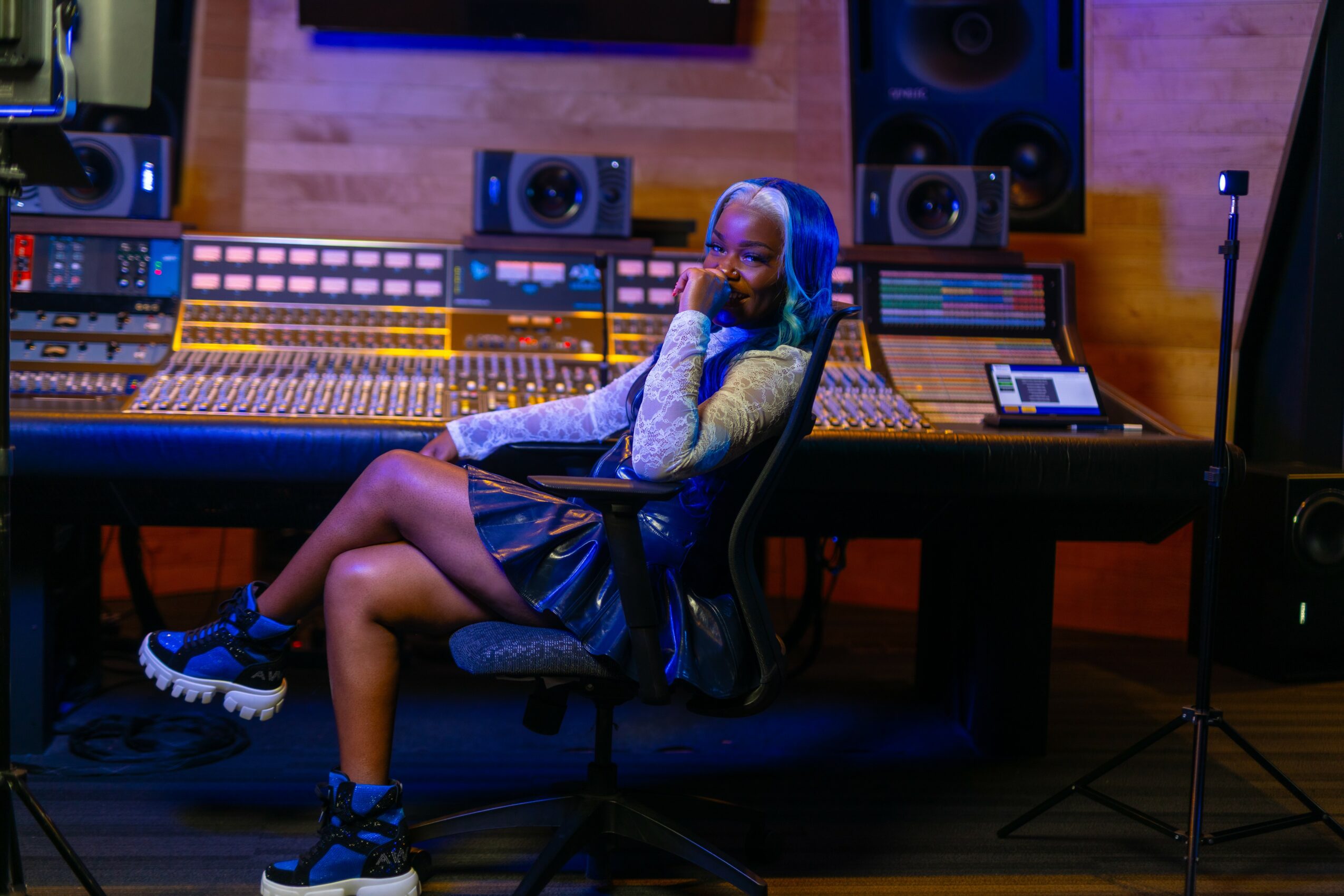 Person sitting in a recording studio with audio equipment and speakers, wearing headphones and a casual outfit.