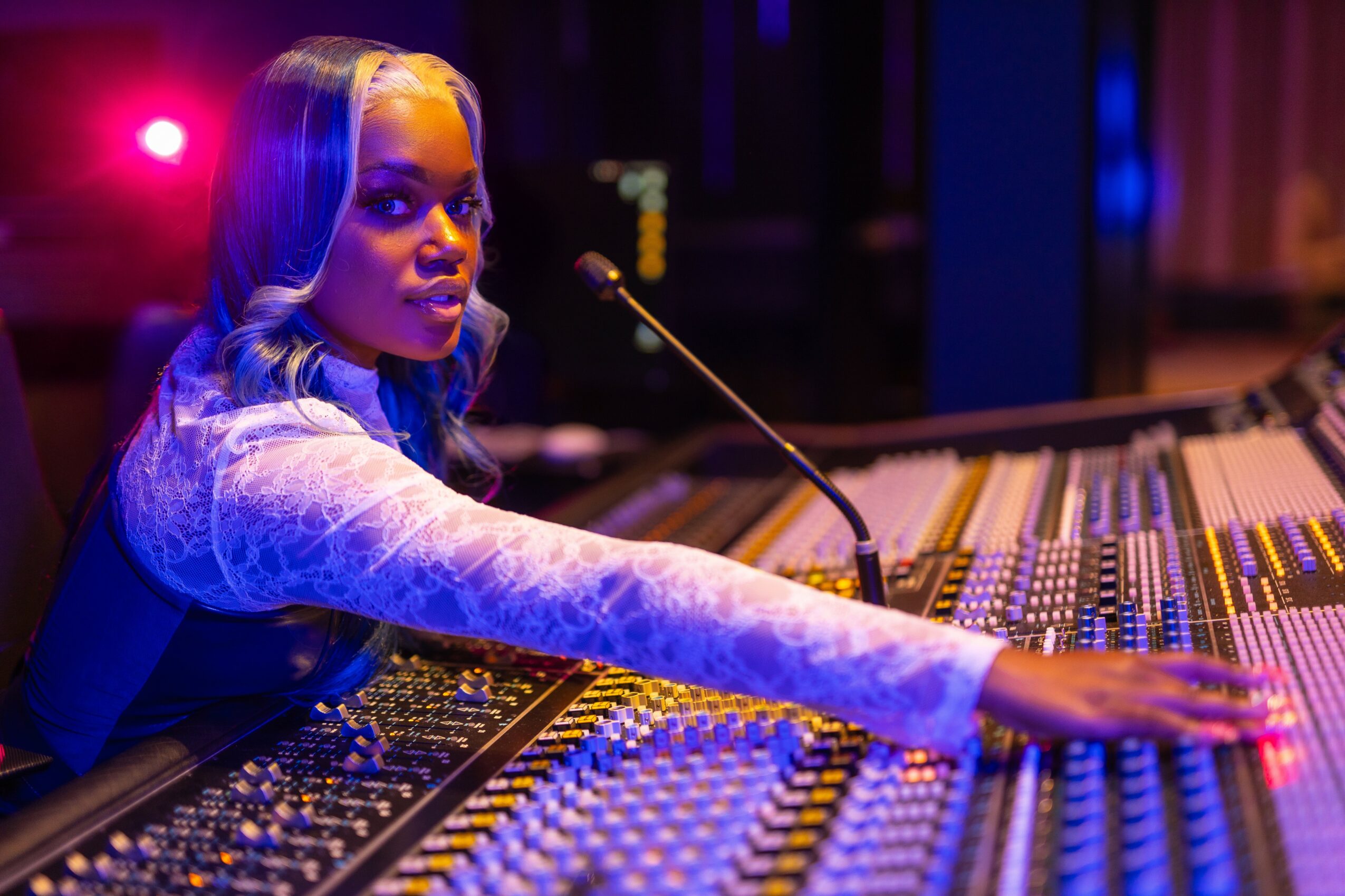 Woman with long hair operating a sound mixing console in a dimly lit room with colorful lights.