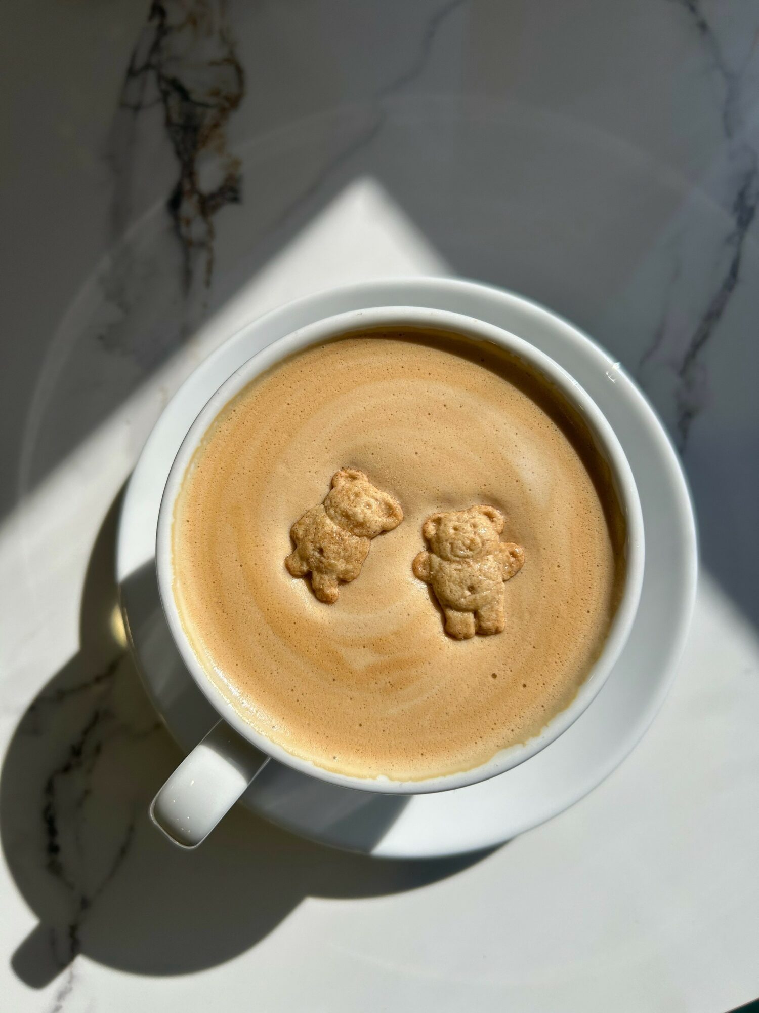 Top-down view of a cup of coffee with bear-shaped foam art, on a marble surface.